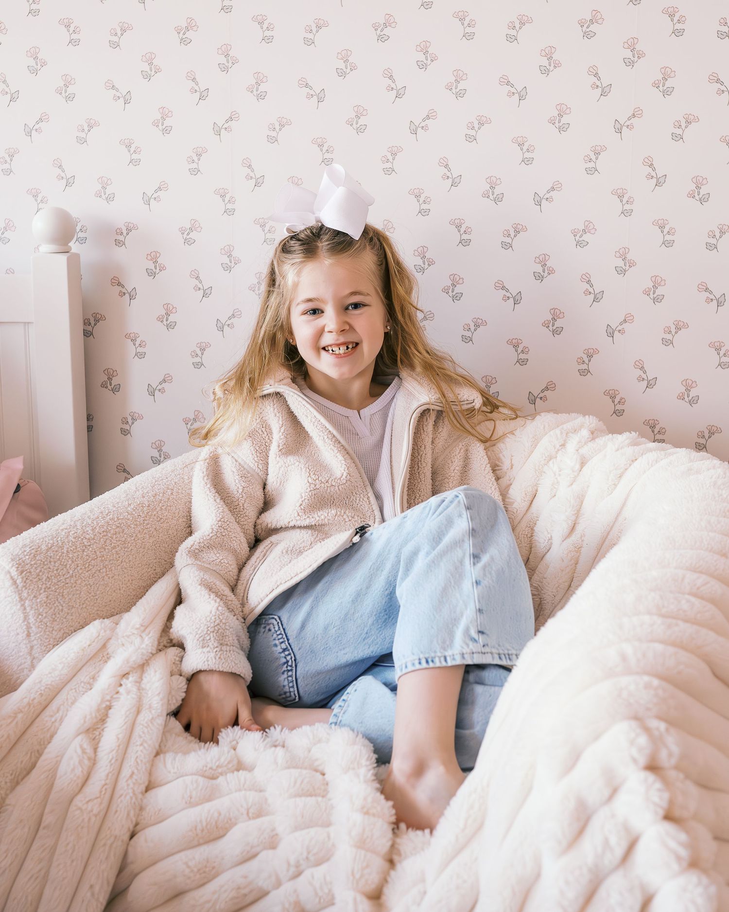 Playful moments on white bedding against delicate floral wallpaper.
