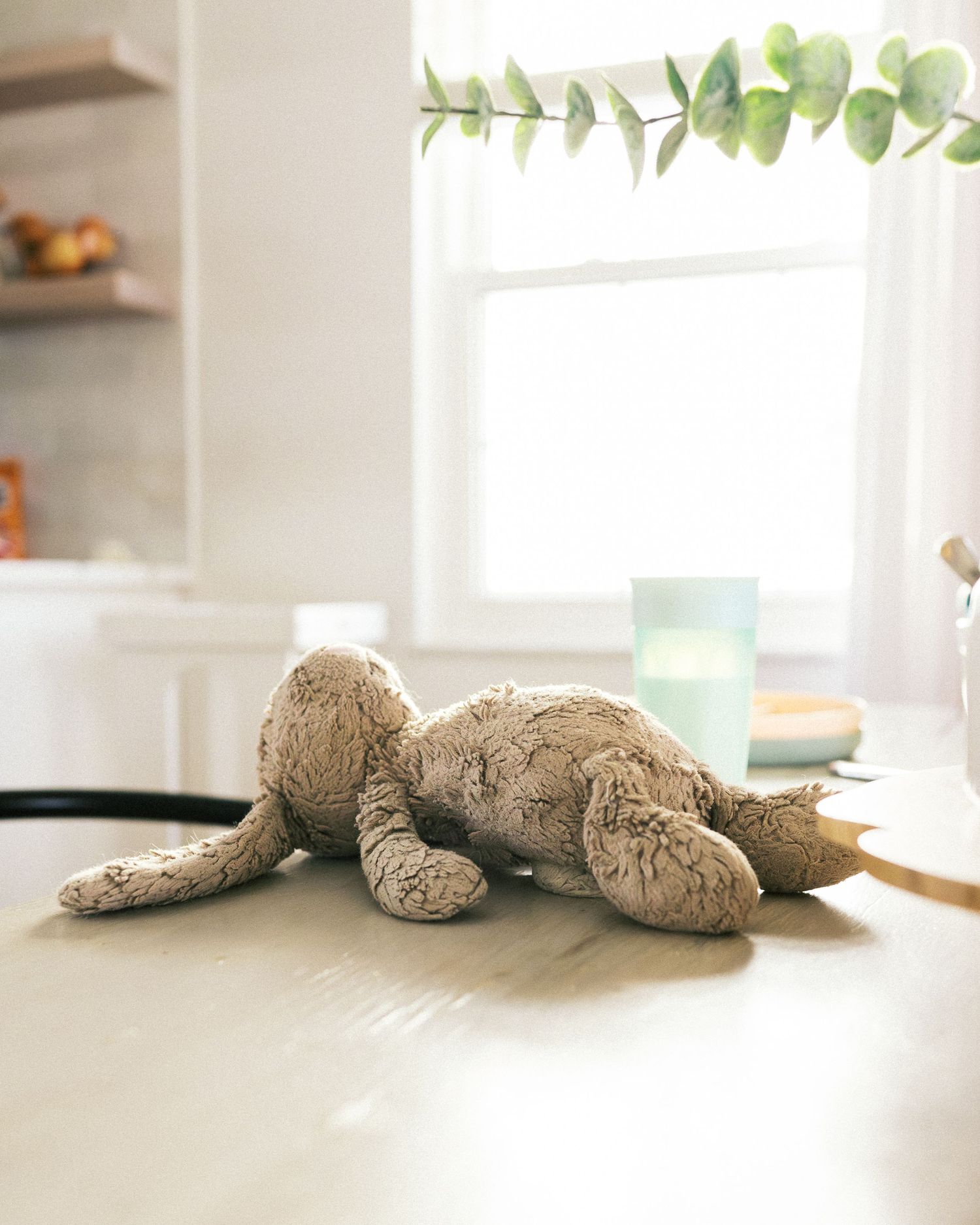 Plush stuffed animal toy lying on white surface near window with natural light.