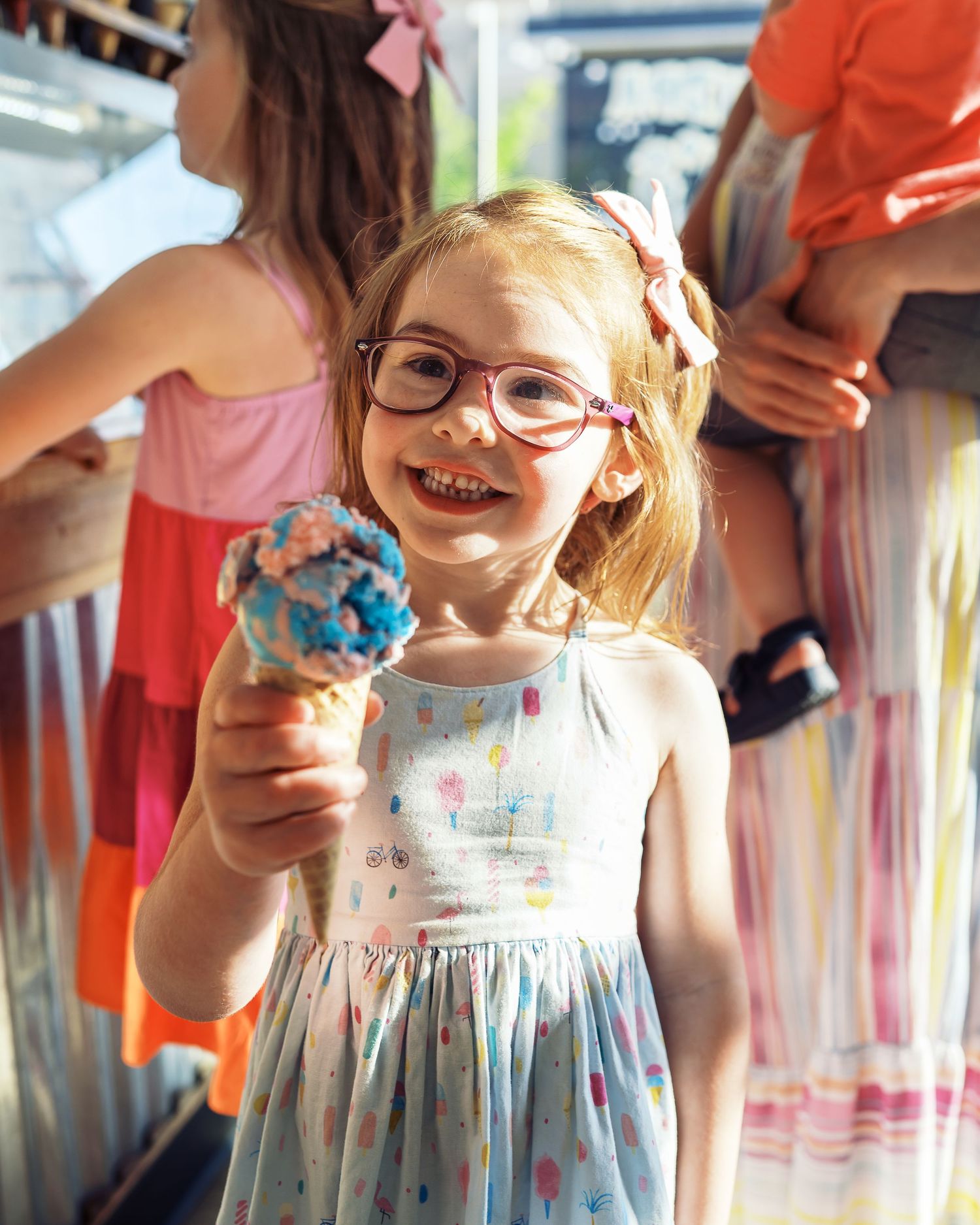 Happy child enjoying a bright blue ice cream cone while wearing a summer dress.