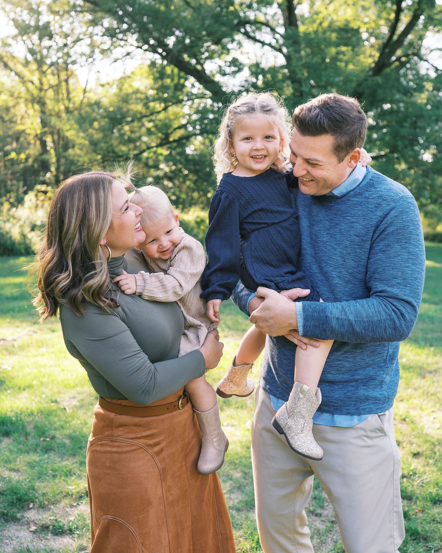 A family shares joyful moments together in a sun-dappled park setting during an outdoor photo session.