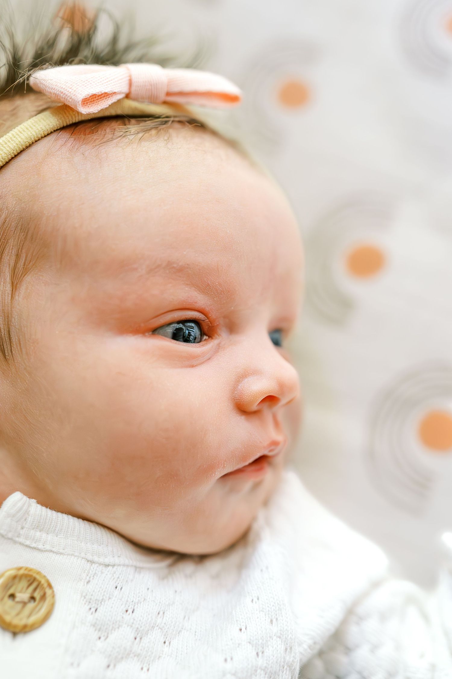 Close-up of baby wearing bow headband against orange patterned background.