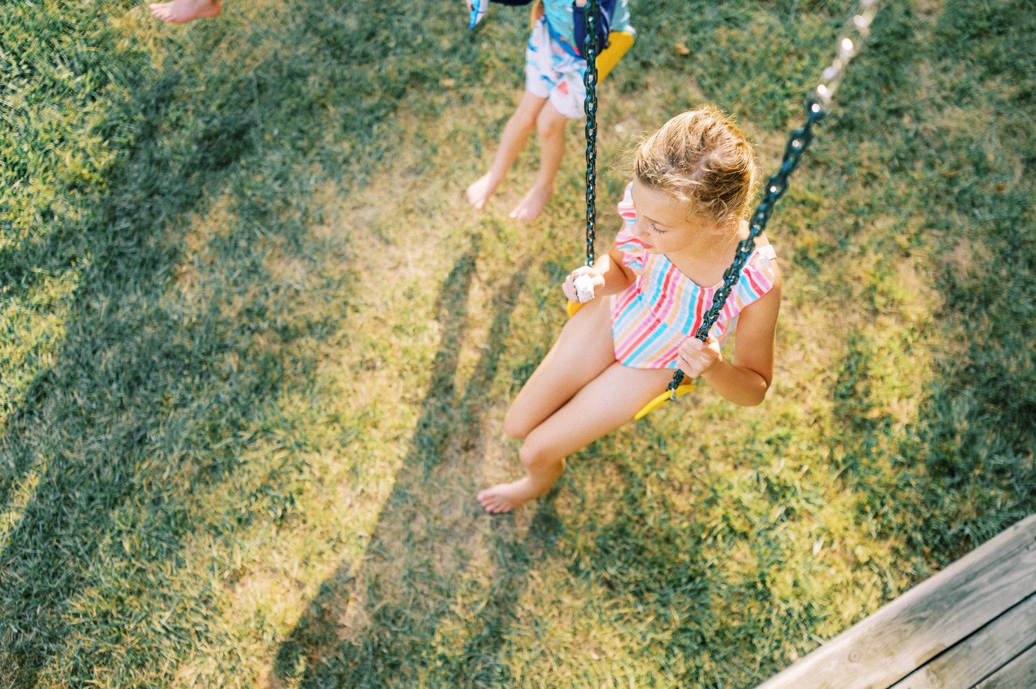 A sunny summer afternoon captured with a child swinging in a backyard play area.