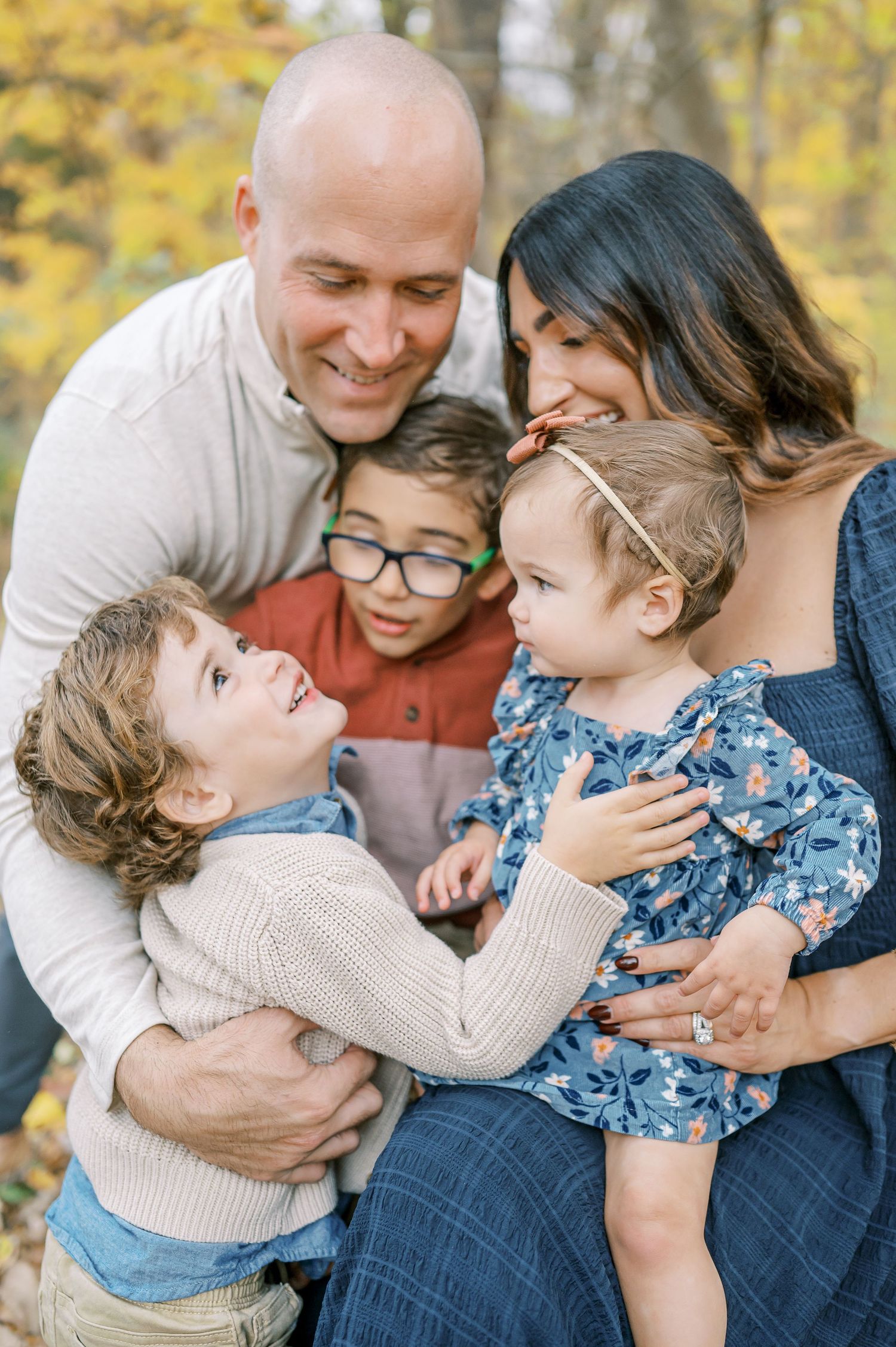 Family shares playful cuddles and laughter while sitting together outdoors in autumn setting.