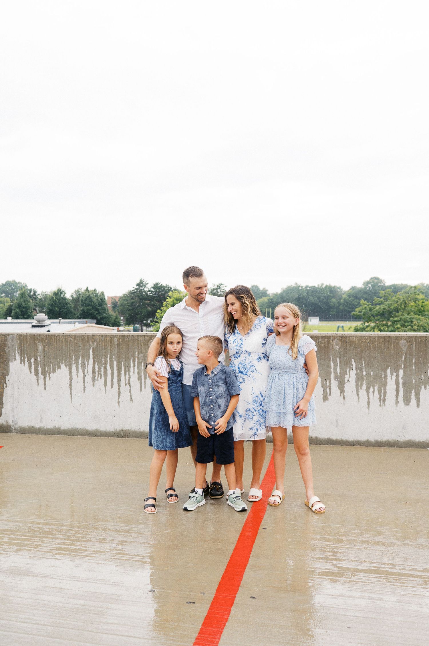 A family walks together on an orange line painted across a wet parking deck surface in warm summer weather.