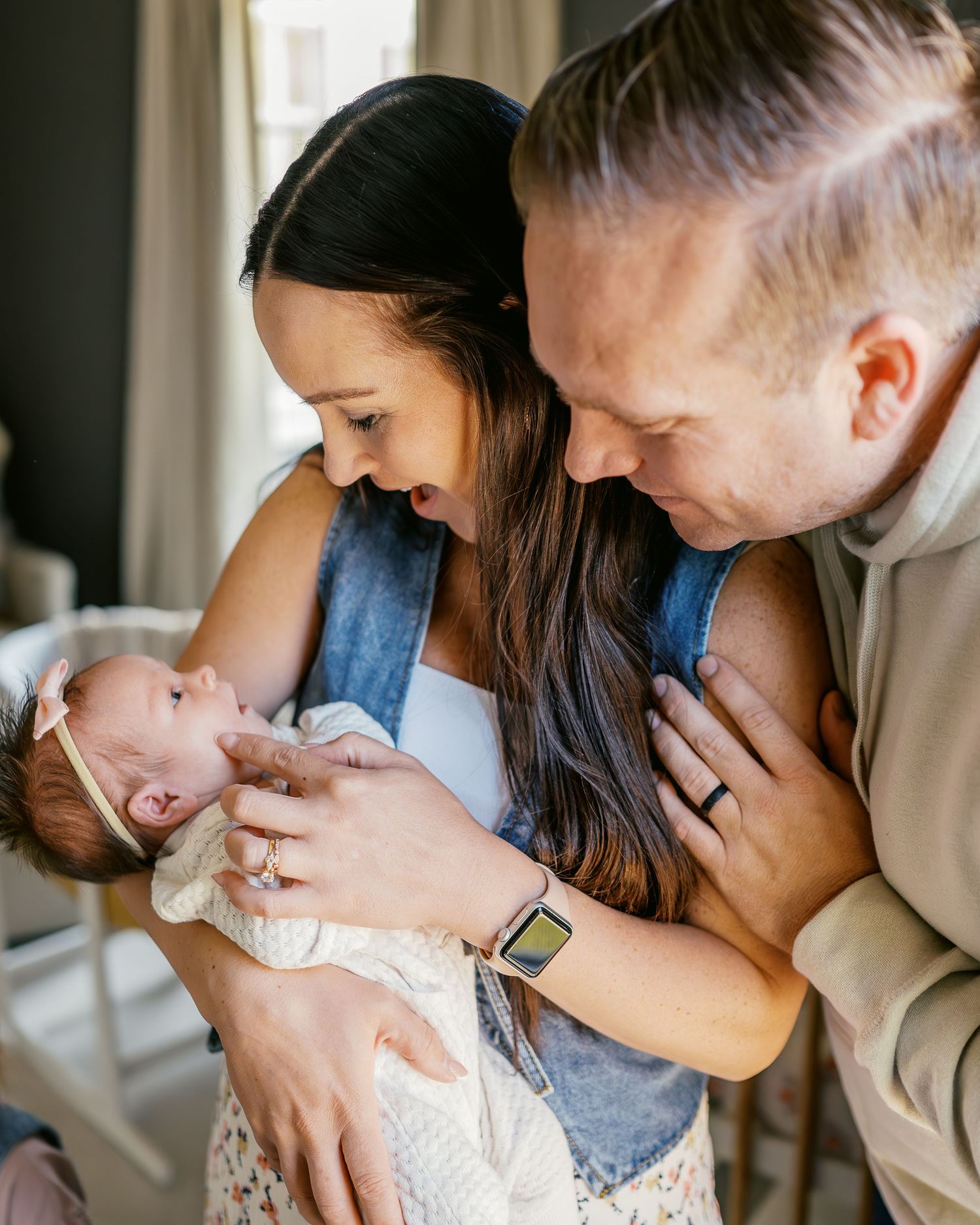Parents share tender moments with their newborn baby in natural window light.