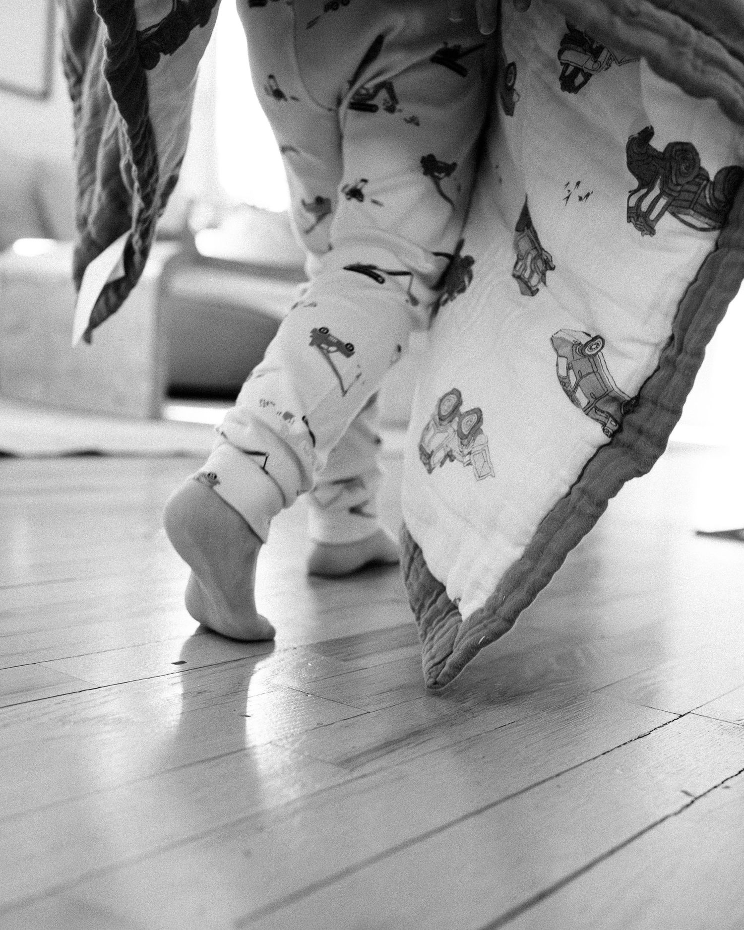 Black and white closeup of small feet in patterned pajamas against wooden floorboards.