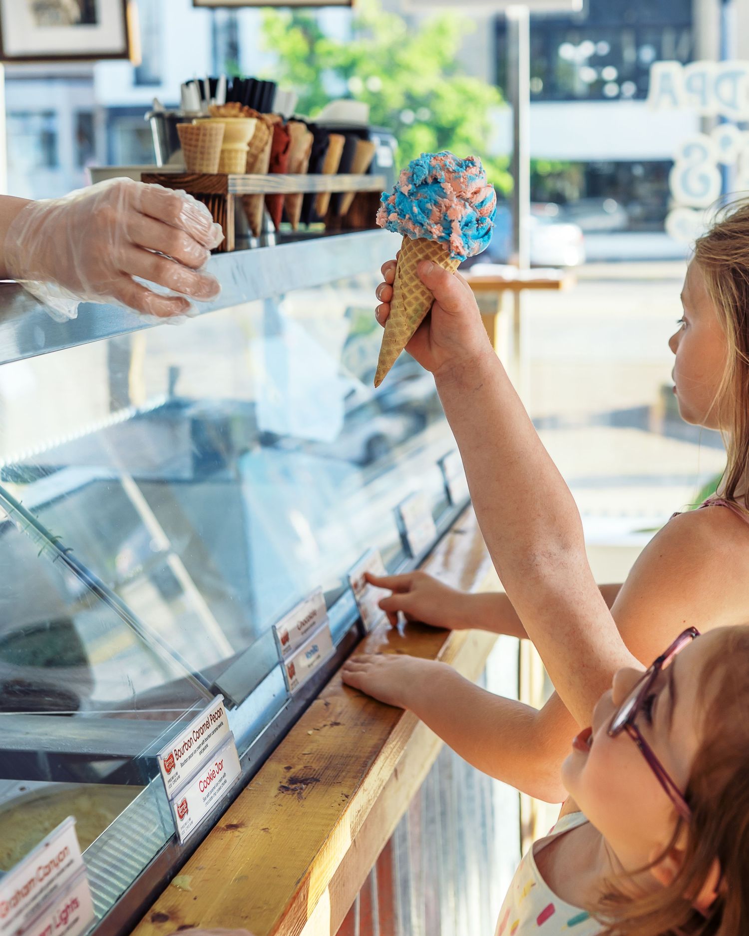 Young customer reaching for a colorful ice cream cone at an ice cream shop counter.
