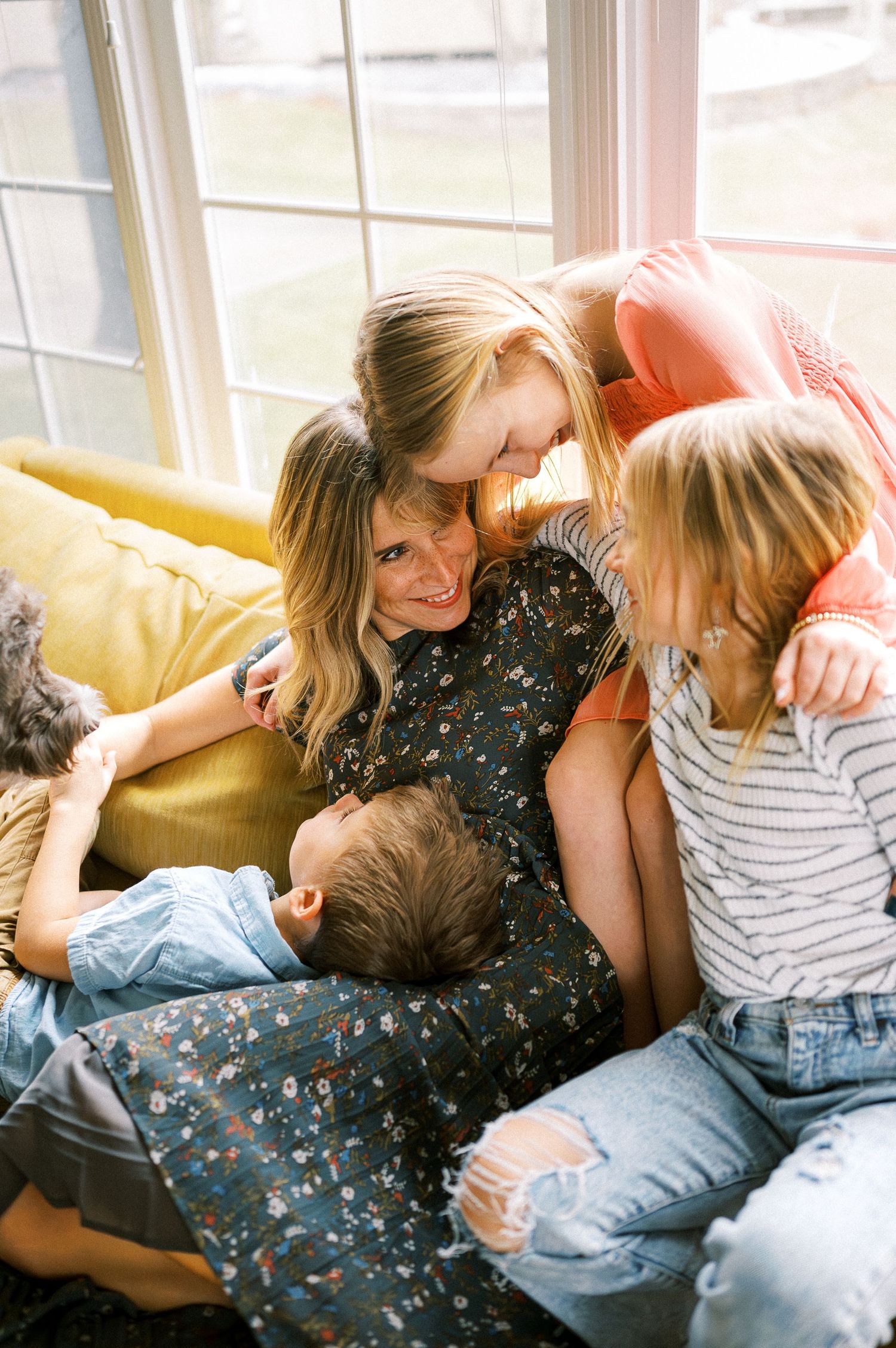 A warm family moment shared on a yellow couch in natural window light.