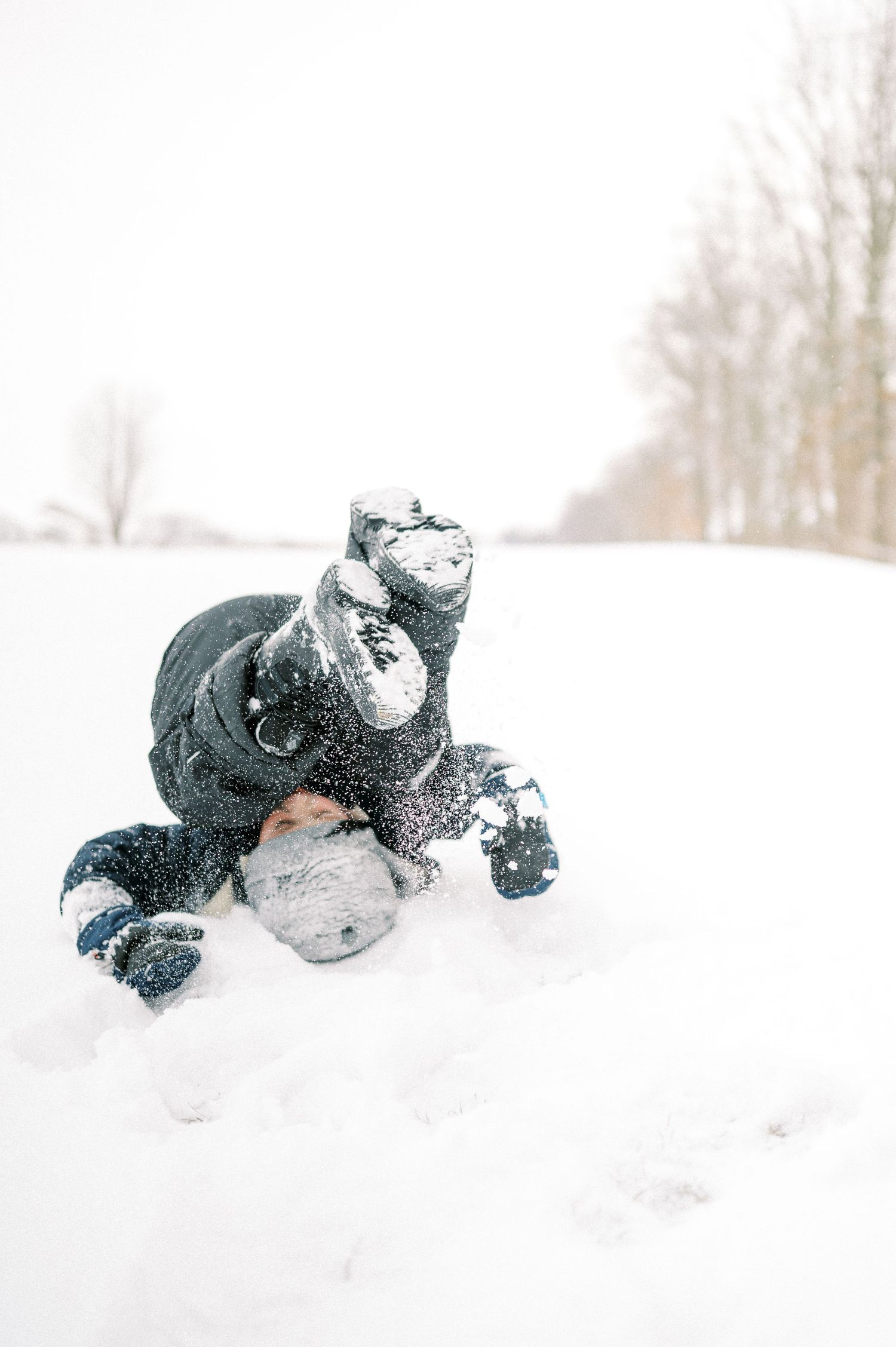 Person falling in deep snow while wearing a black winter coat.