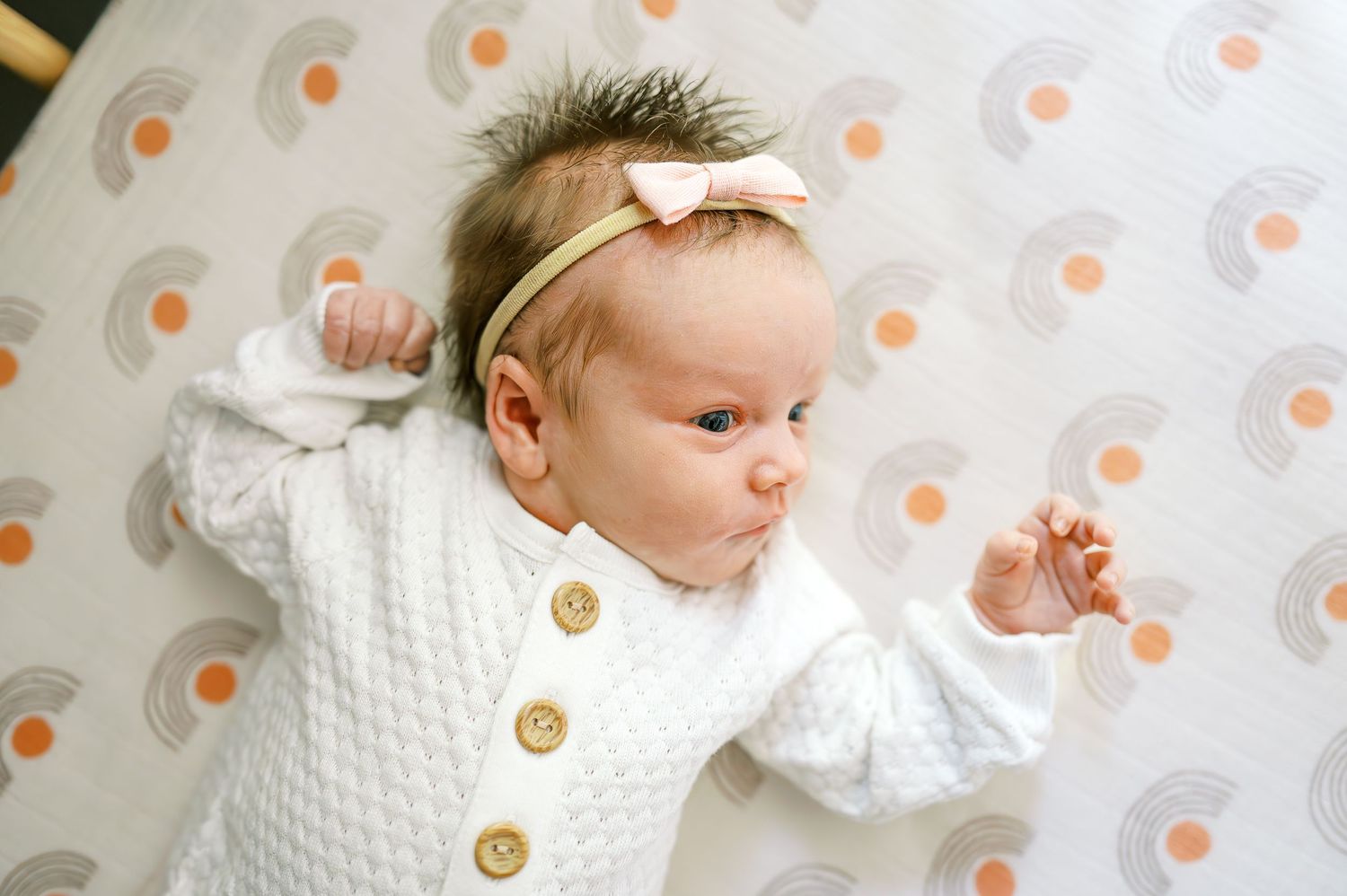 Baby wearing white sweater with wooden buttons on patterned fabric.