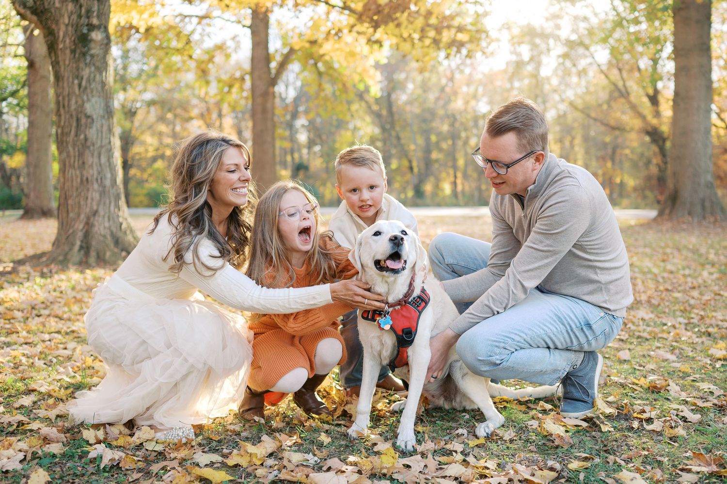 Family playing and having fun together on fallen autumn leaves with their white dog.