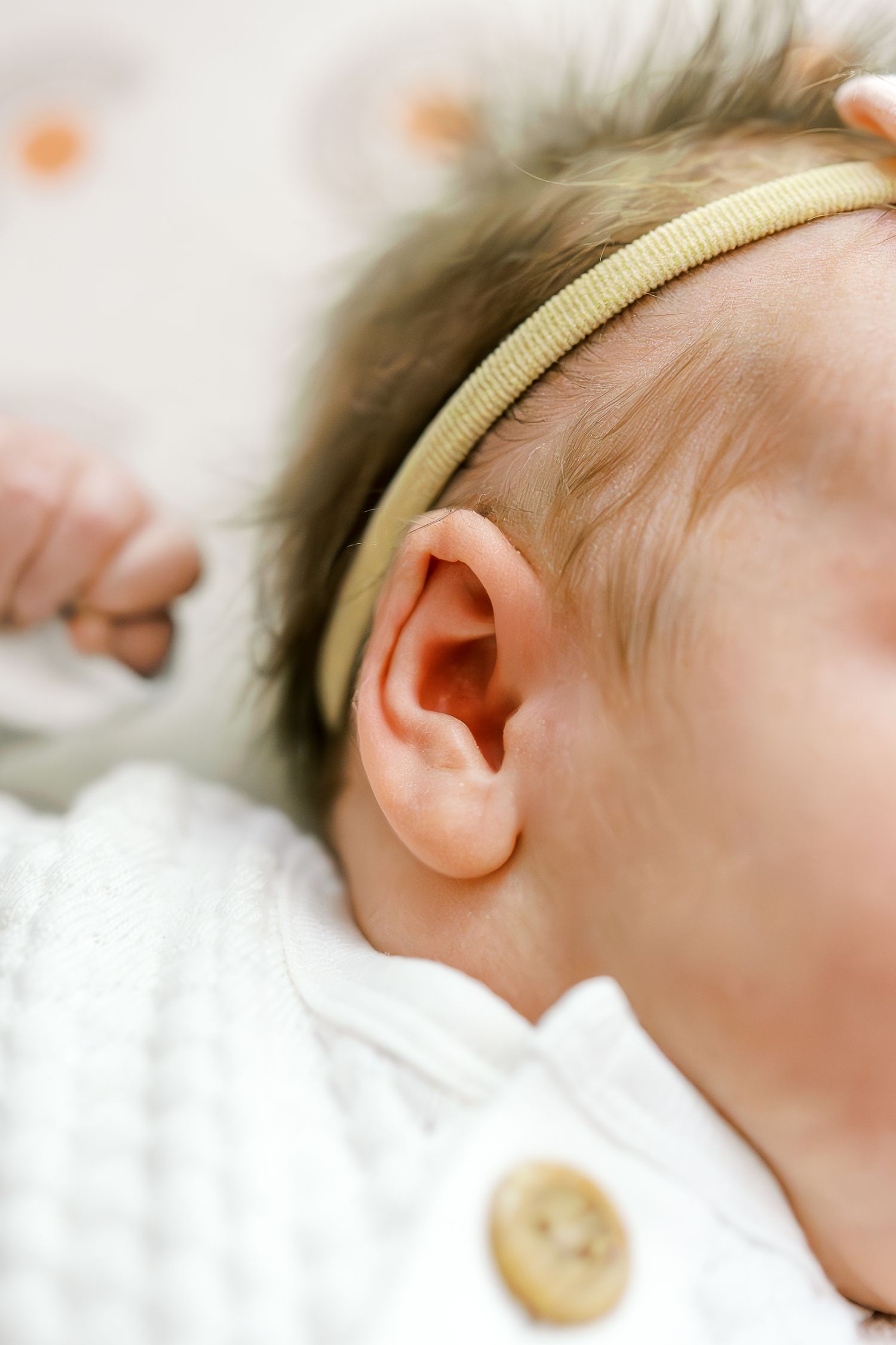 Close-up detail of baby's ear with yellow headband against patterned background.