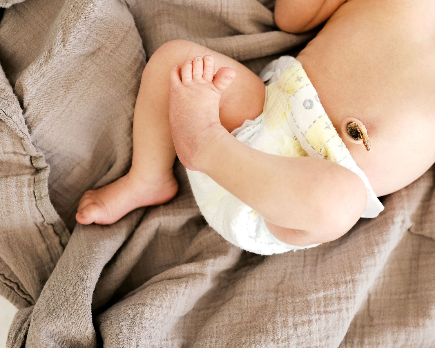 Close up of baby feet and diaper against neutral colored fabric.