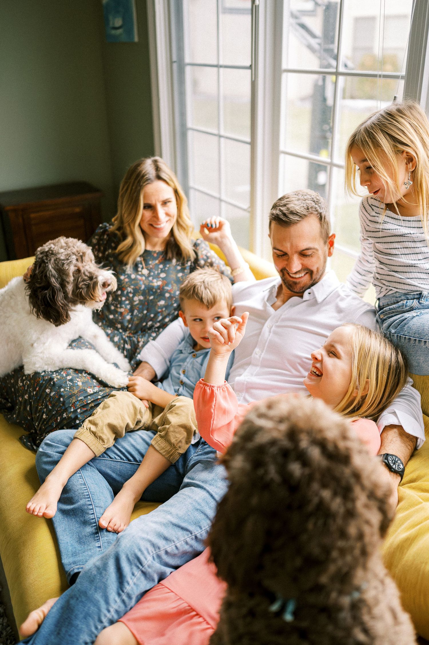 Joyful family scene with dog lounging together on yellow sofa.