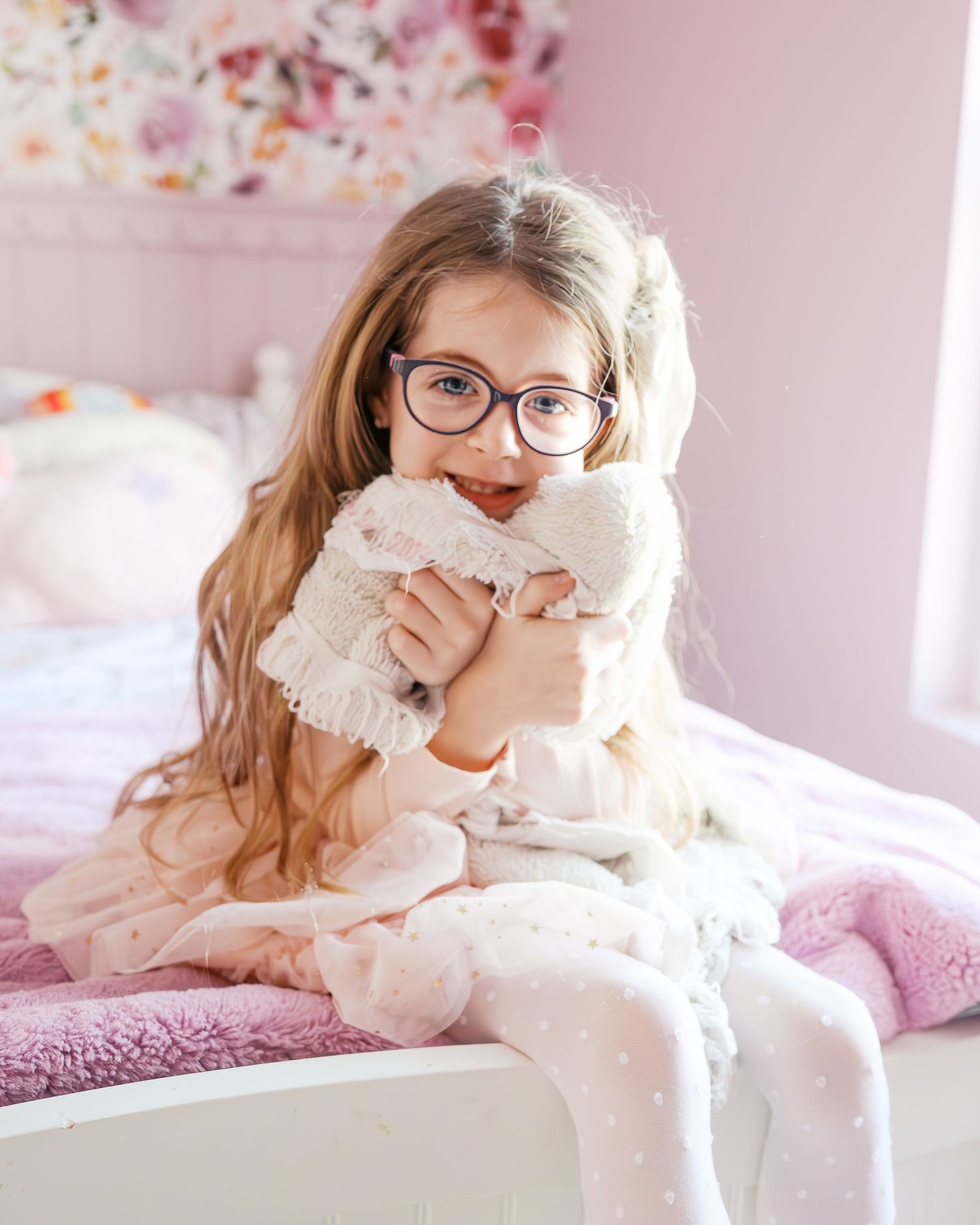 Gentle moments captured in pink bedroom with soft lighting and white bedding.