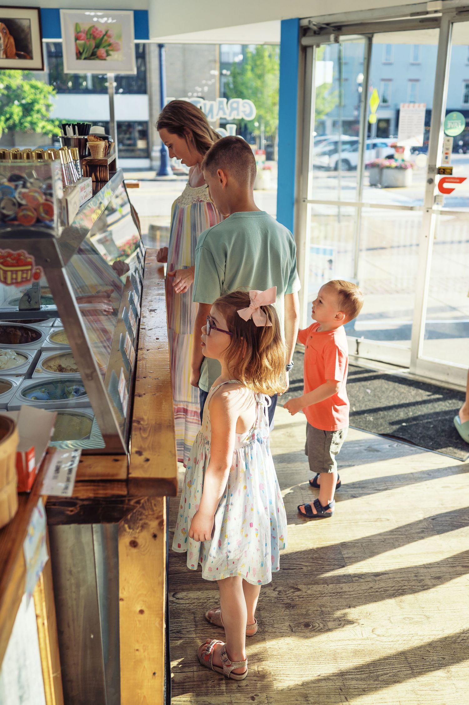 Customers browsing items at an ice cream shop counter on a bright summer day.