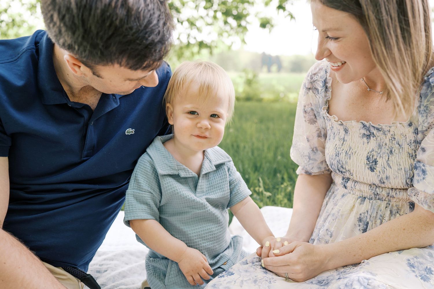 A family sitting together on a blanket in a sunny field wearing coordinating blue outfits.