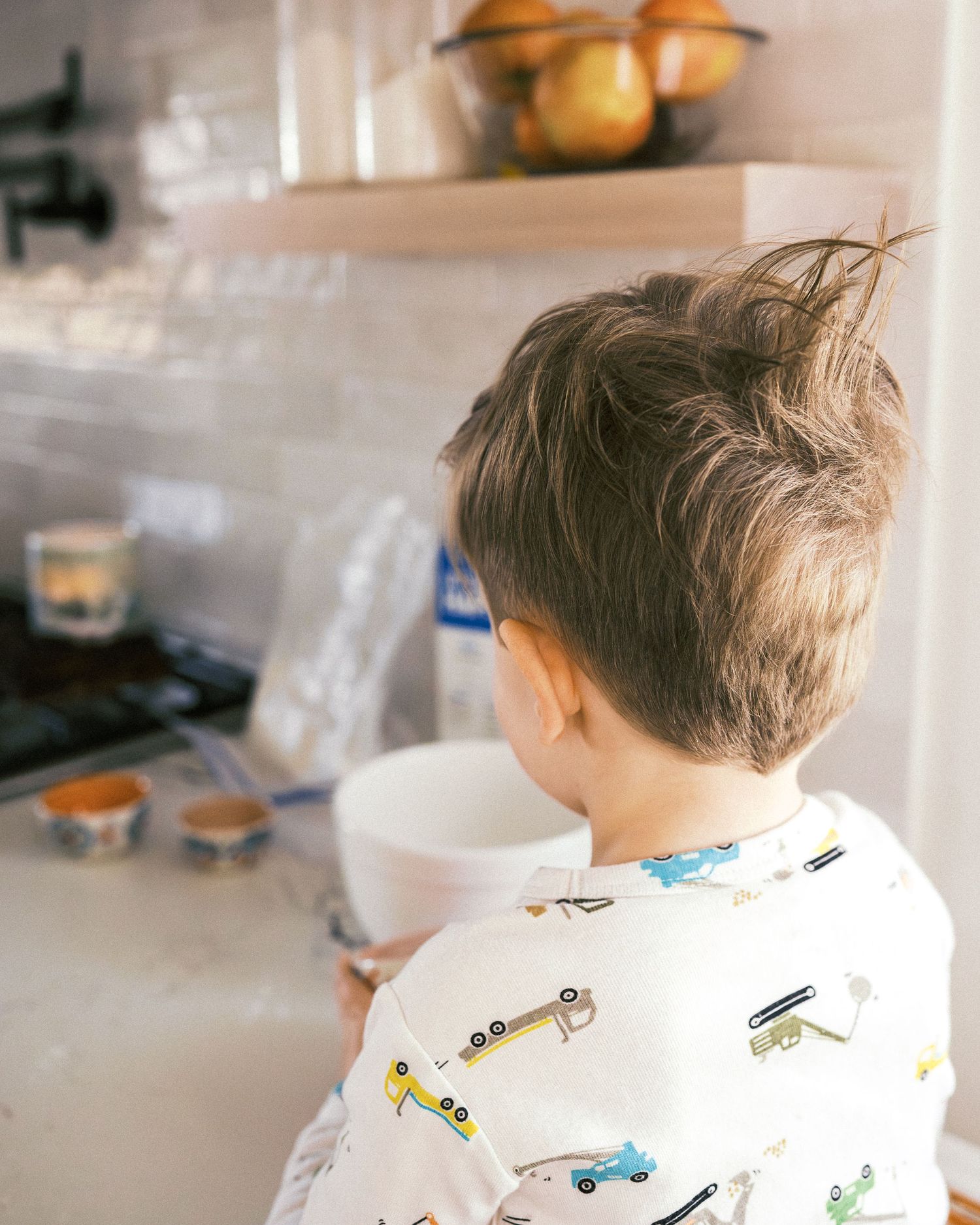 Child's profile view showing messy hair while standing in a kitchen with containers in background.