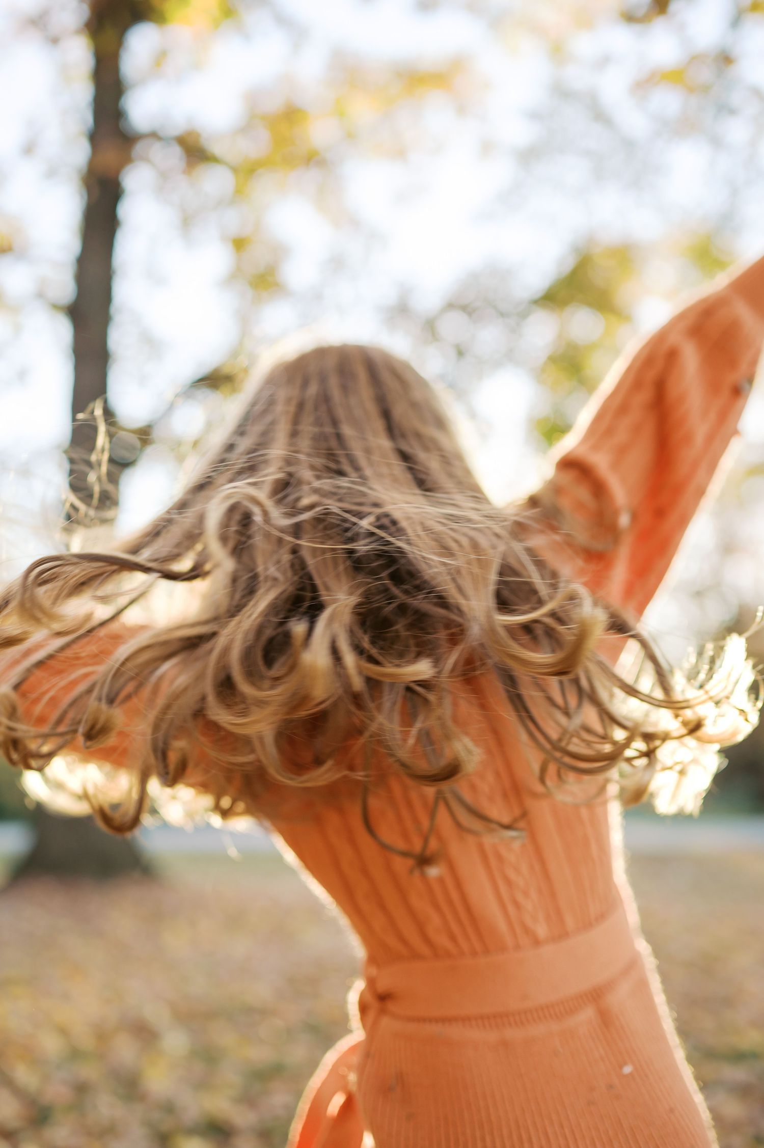 Person with flowing hair spinning in an orange dress against golden autumn trees.