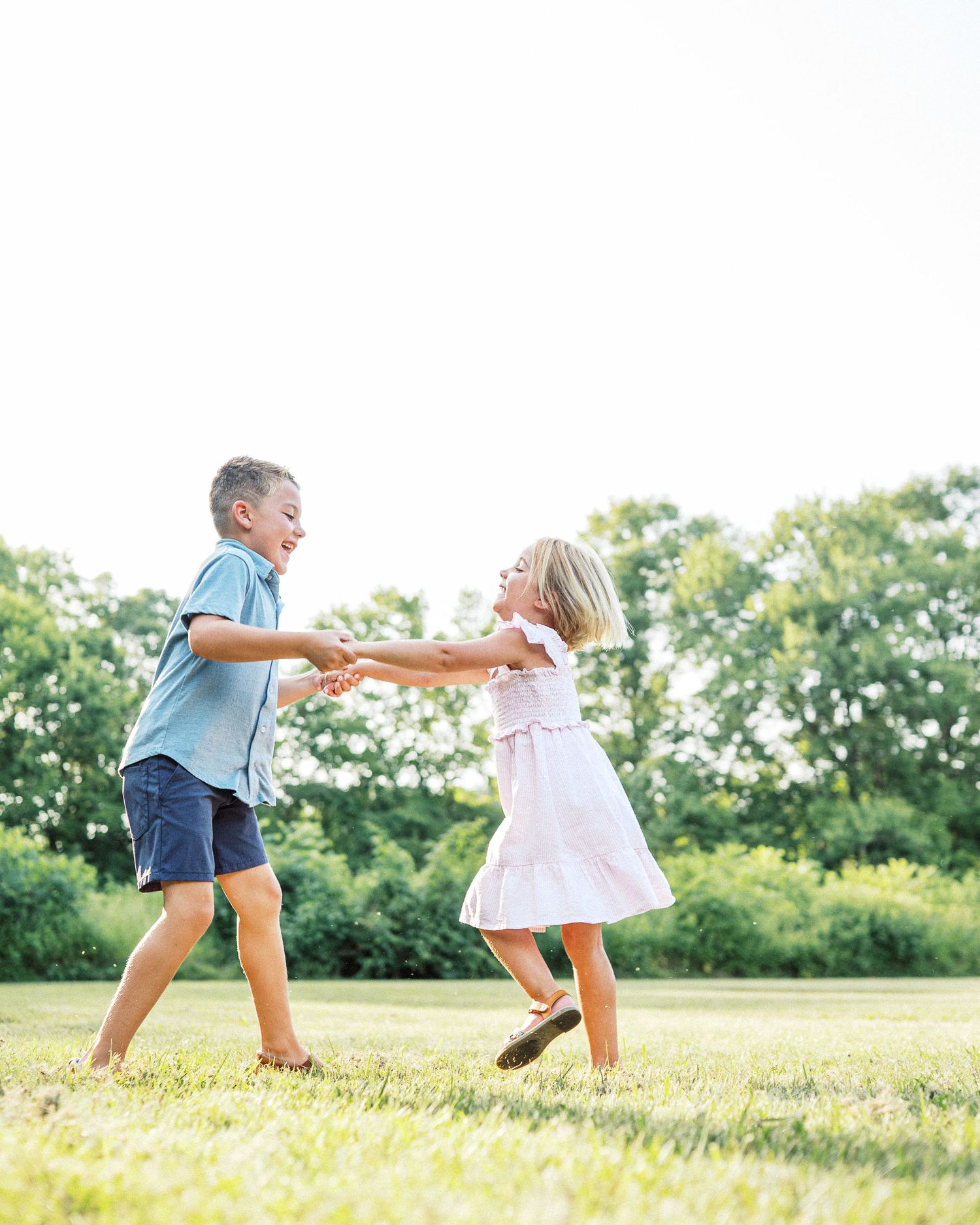 Two children playing and holding hands while dancing in a sunlit field.