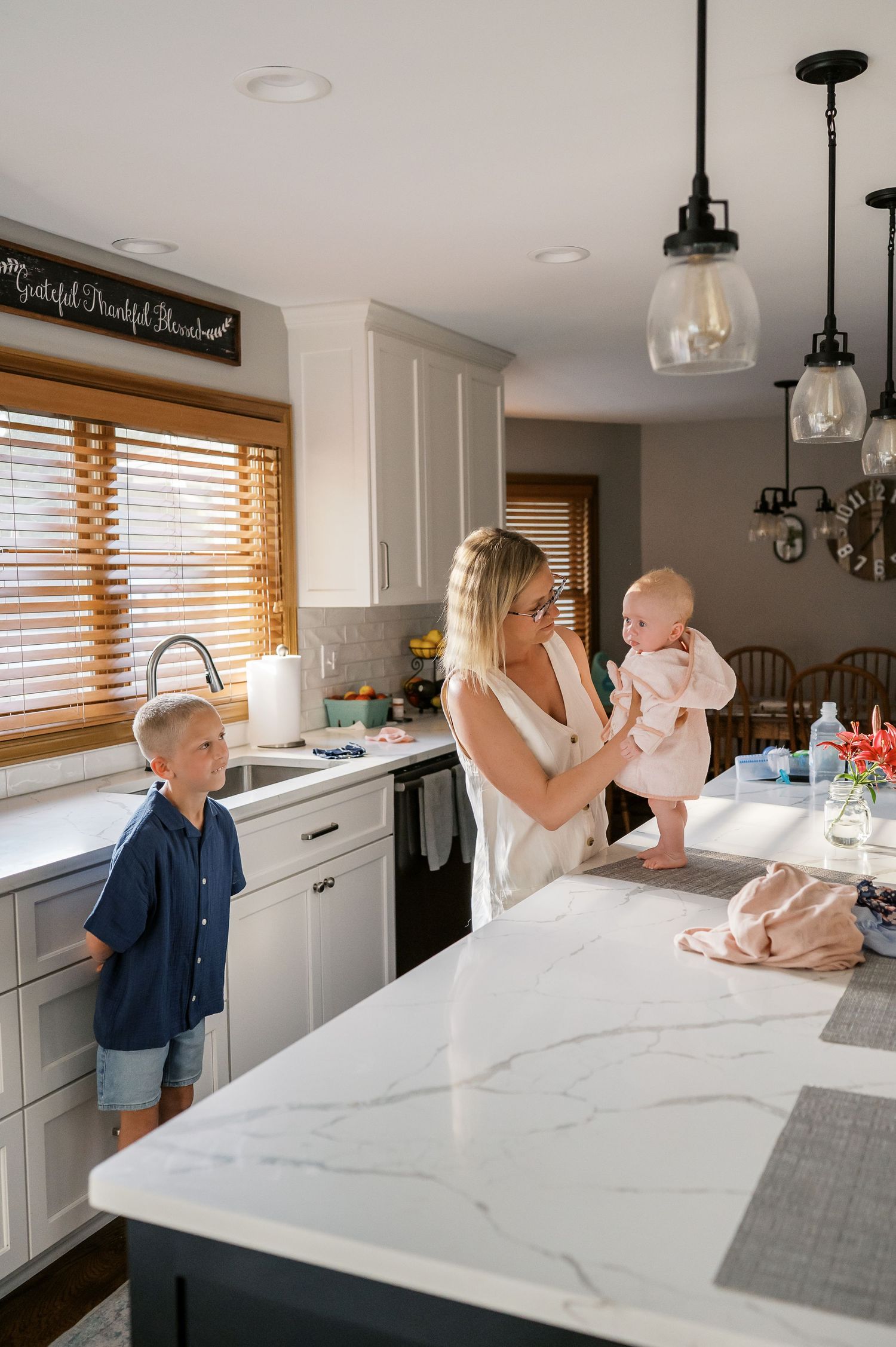 Modern kitchen scene with marble countertops and pendant lighting.