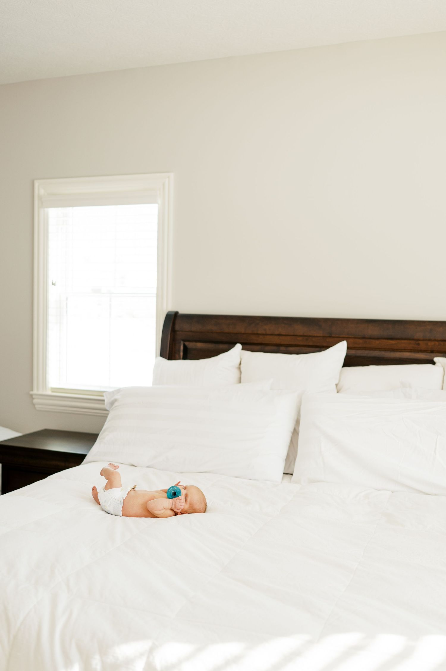 Small baby resting on white bedding in bright minimalist bedroom.