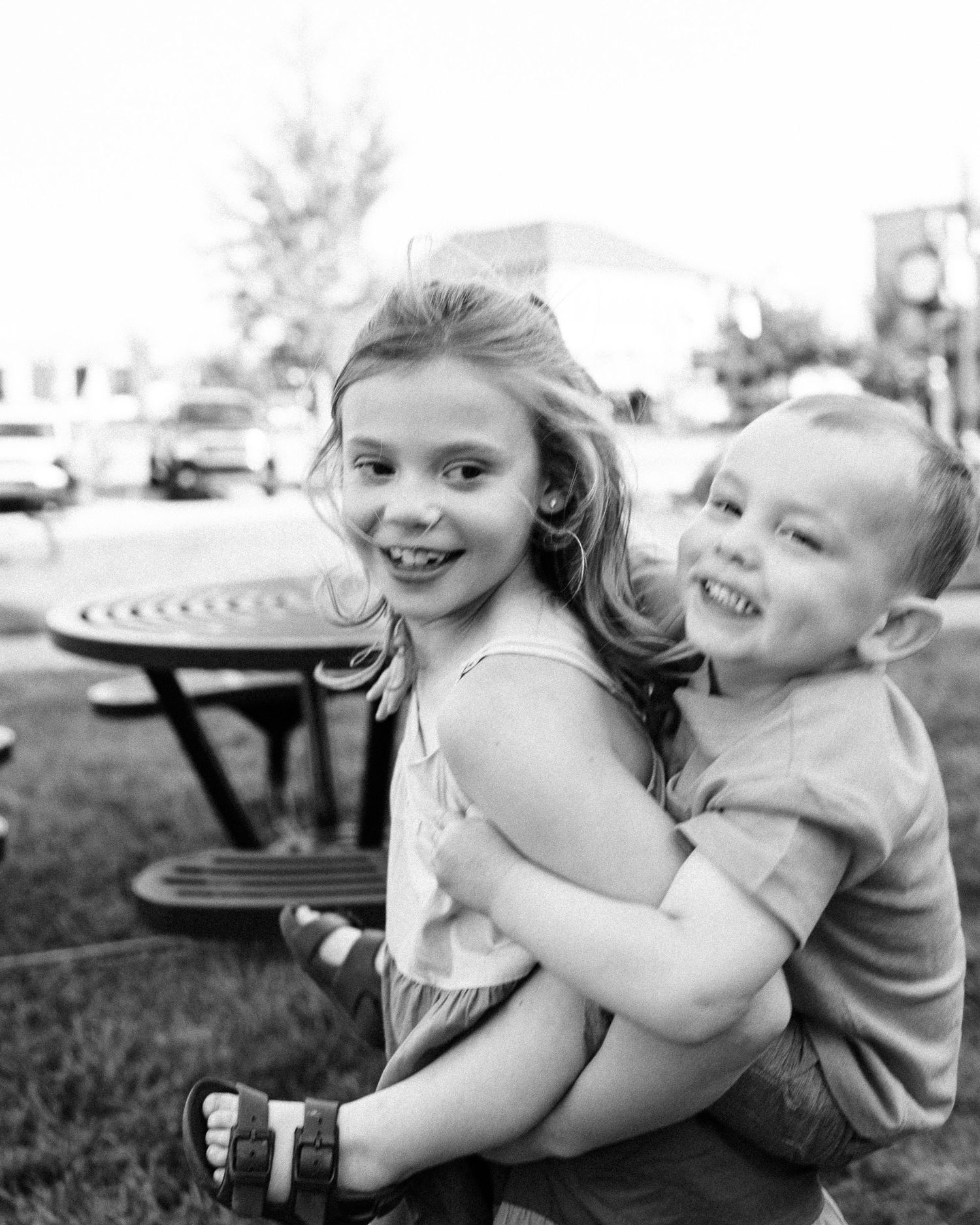 Black and white candid shot of children sharing a lighthearted moment outdoors.