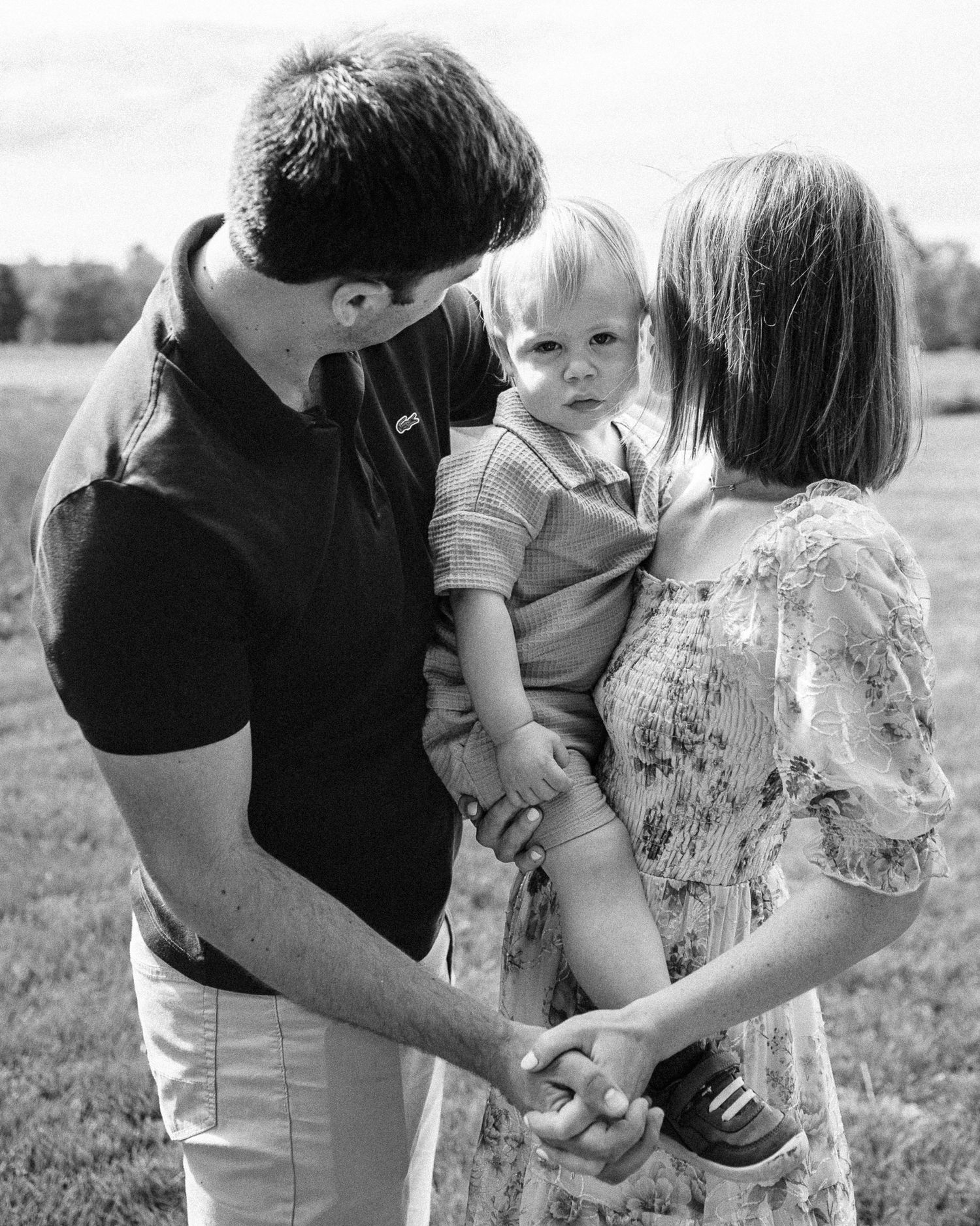 Black and white portrait of family holding hands together in field.