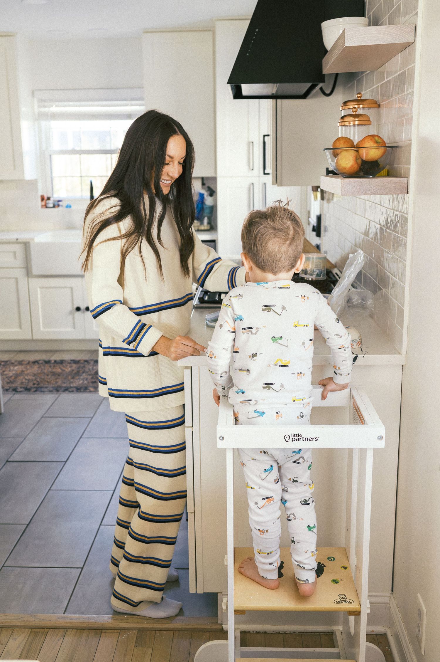 Parent and child matching in striped pajamas bake together at a white kitchen counter.