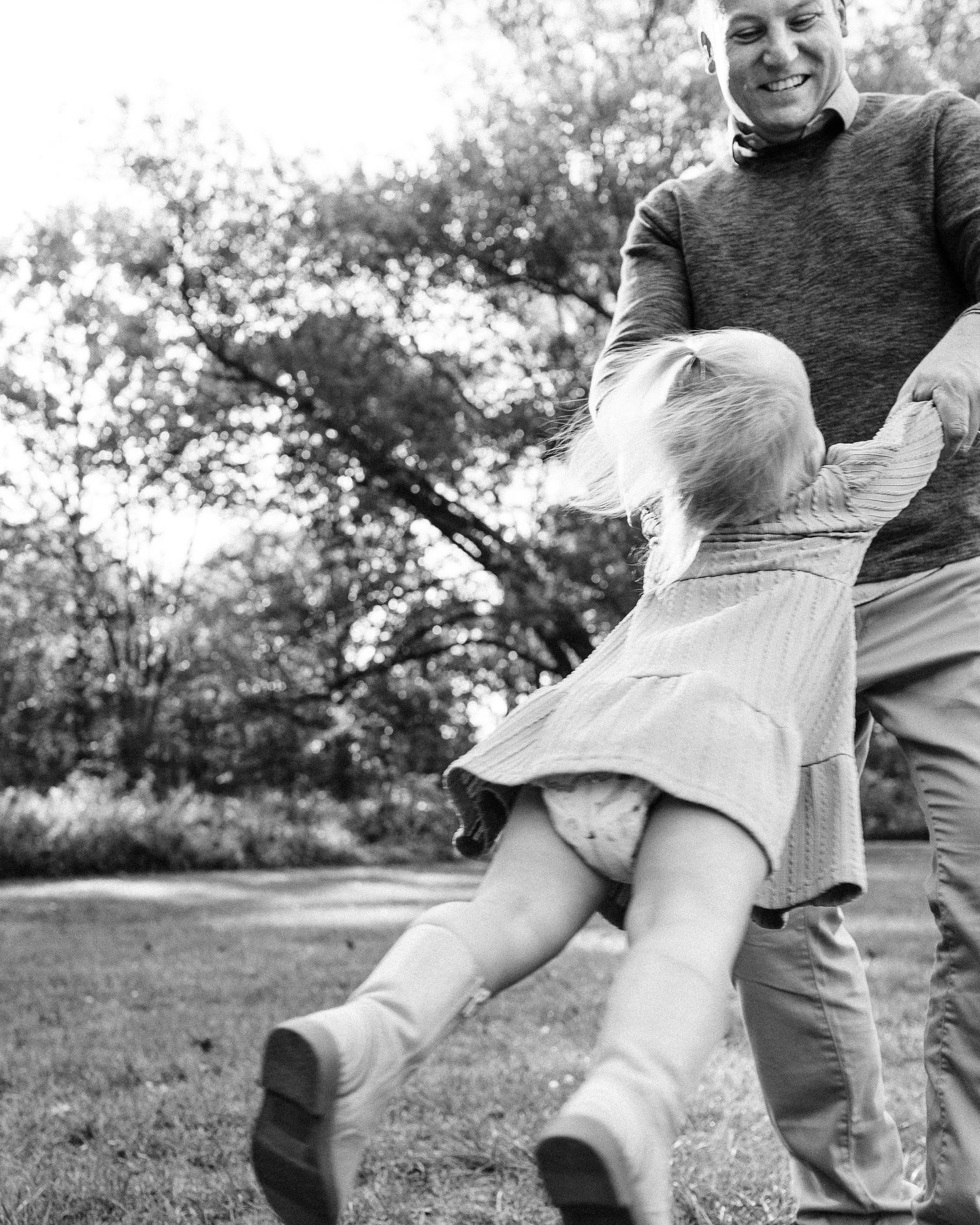 Black and white sequence of photos showing a person playfully spinning and falling on grass in an outdoor setting.