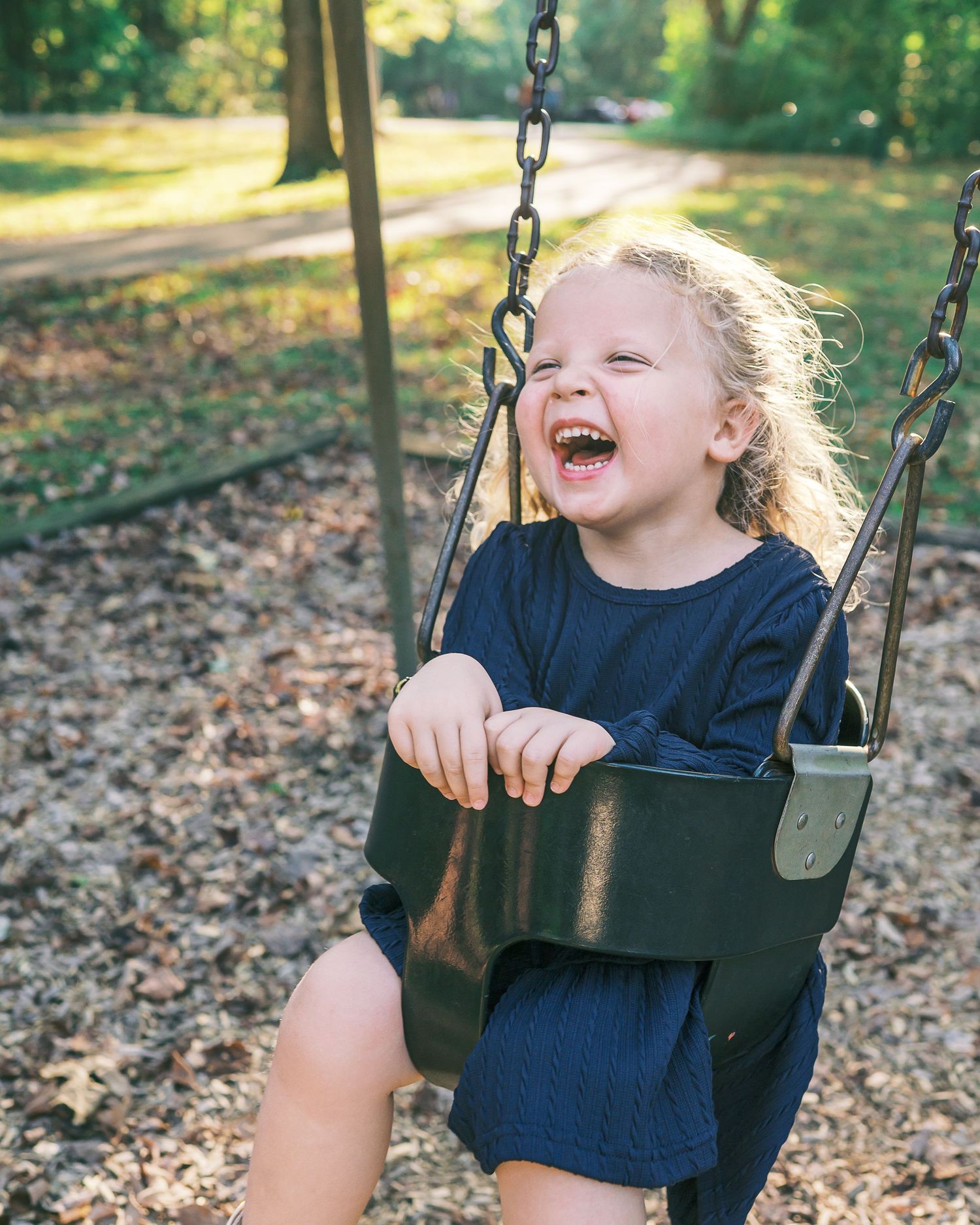 A child enjoying a swing ride outdoors on a sunny autumn day, expressing pure joy and laughter.