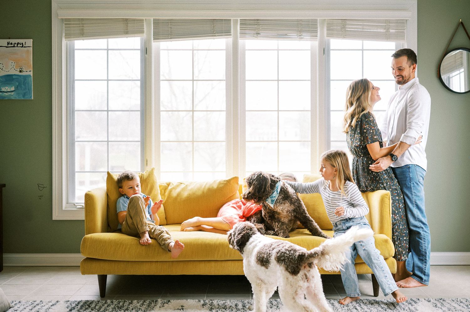 Natural light streams through windows as family members play and bond on their yellow sofa.