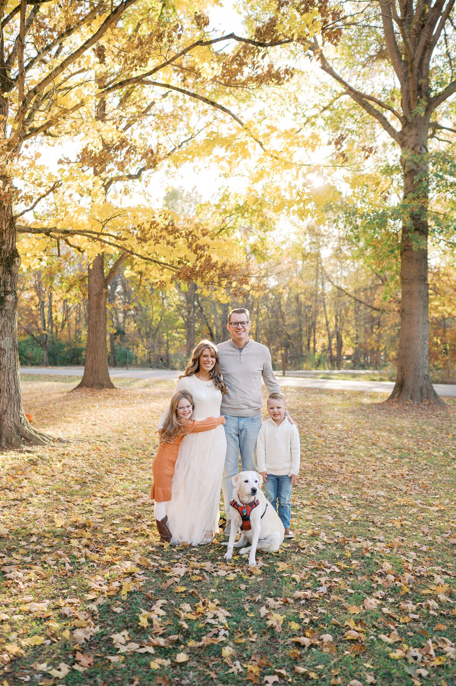 Candid family photo in a park during fall with colorful autumn leaves scattered on the ground.