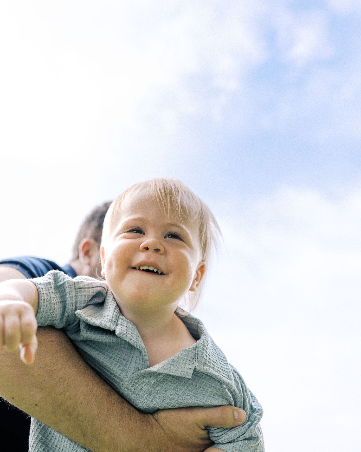 Happy toddler being held up against blue sky background.