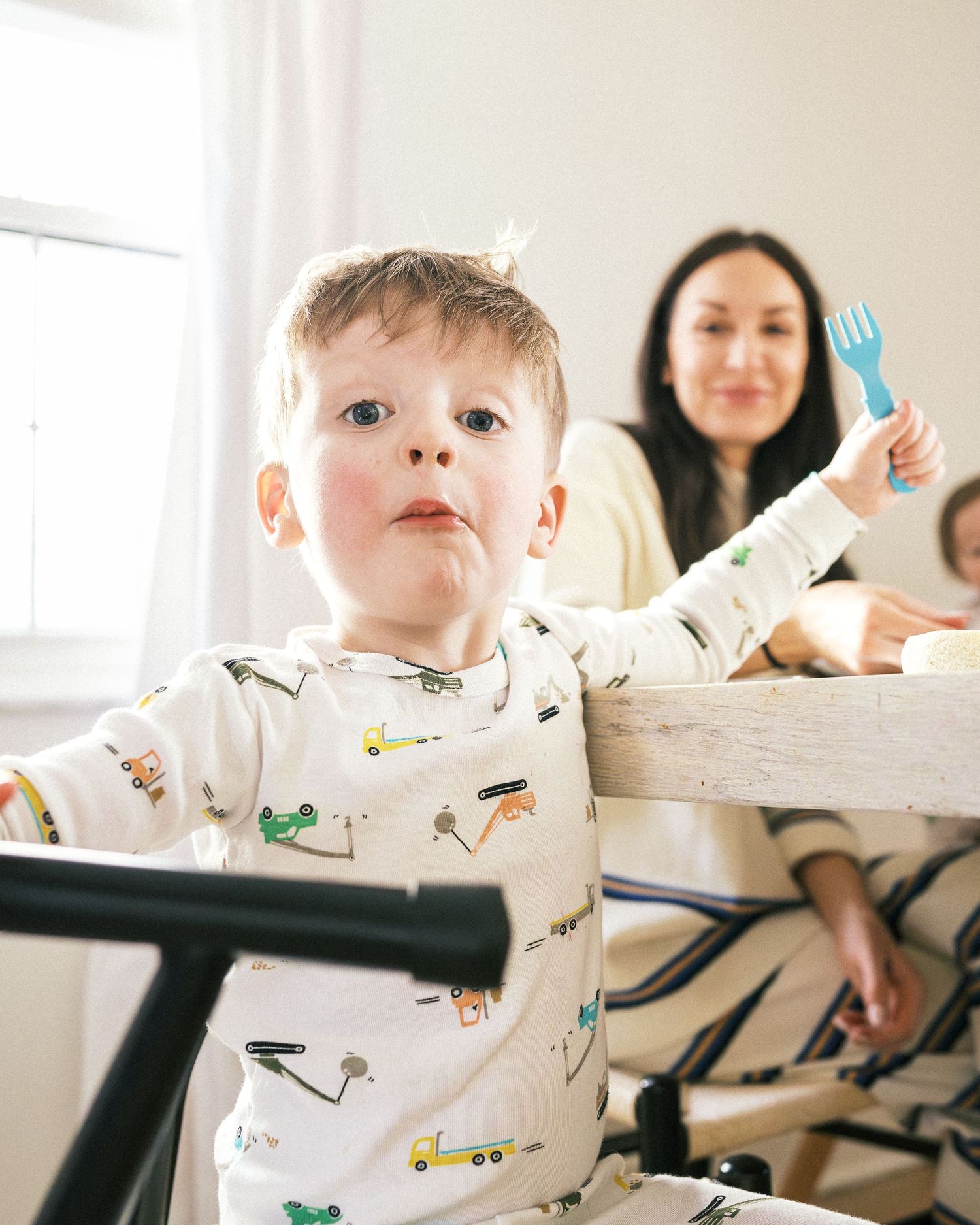 A child wearing a white patterned outfit sits in a high chair during mealtime.
