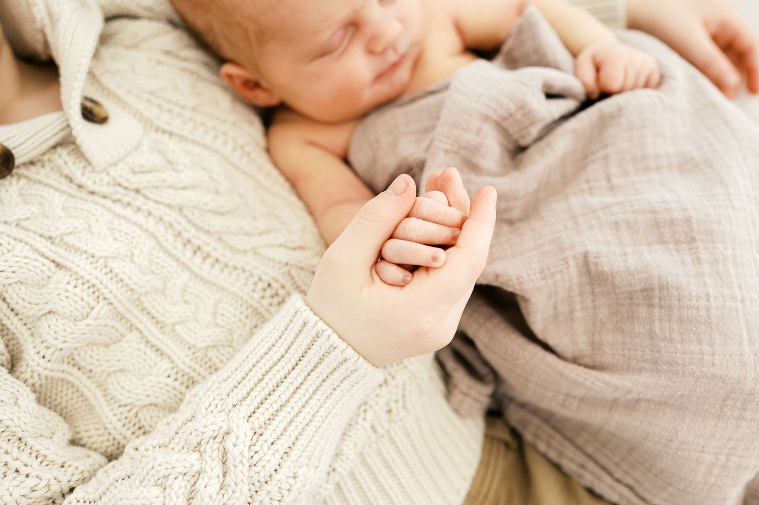 Close up of a tiny baby hand being held against a knit sweater.
