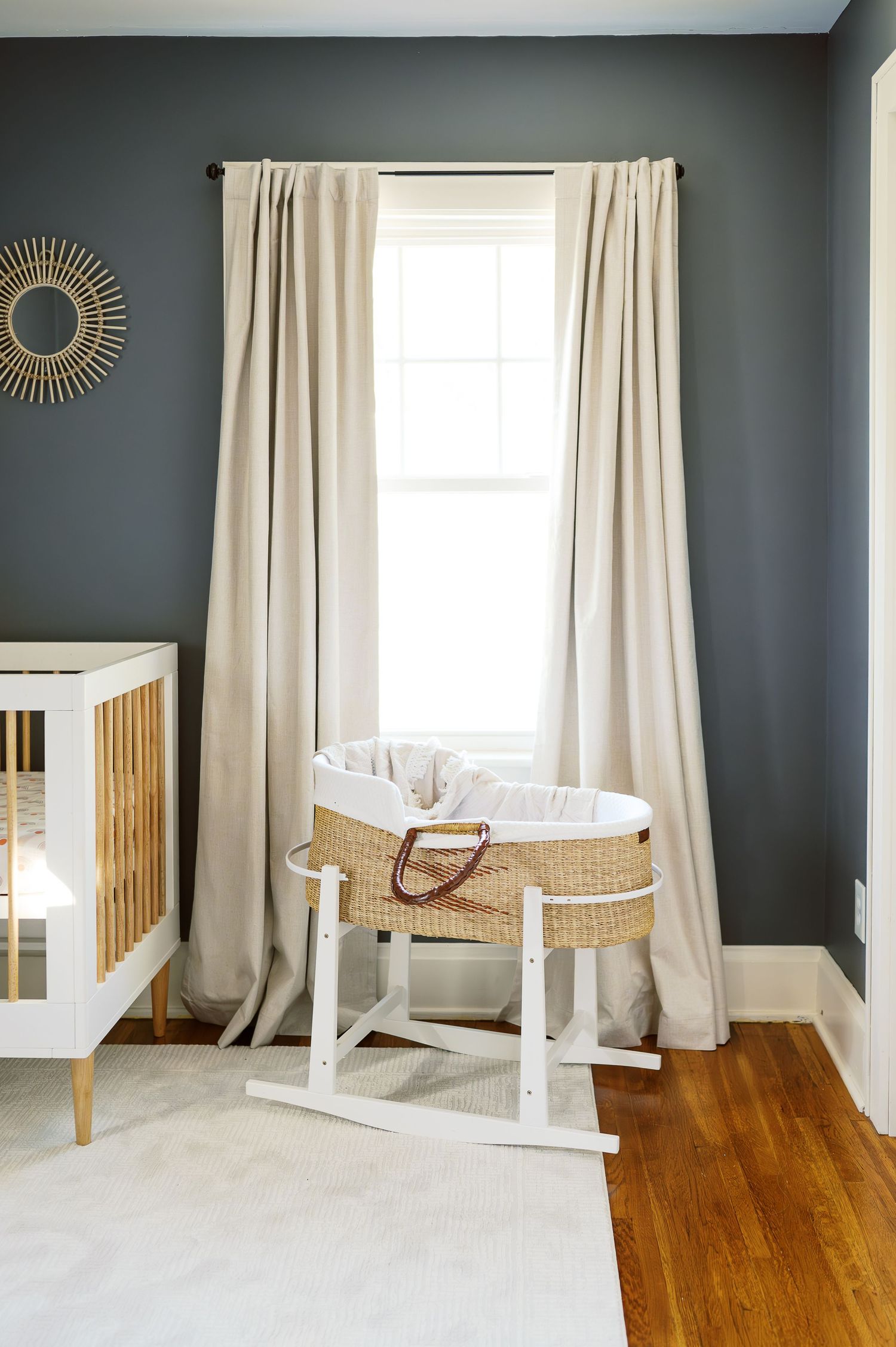 A modern nursery corner with gray walls, white curtains, and a Moses basket on a stand.