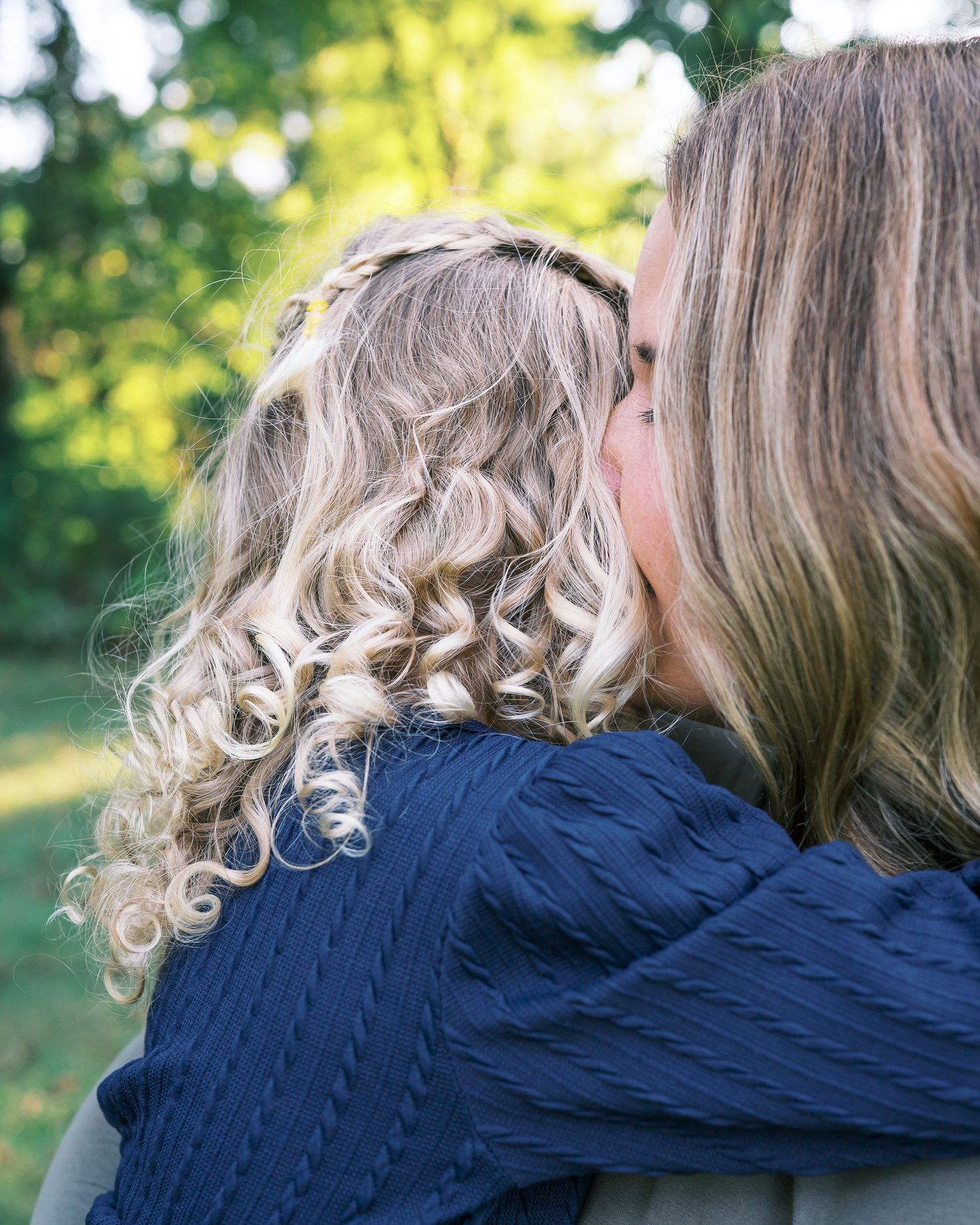 Close-up of curly blonde hair against navy blue fabric in natural outdoor lighting.