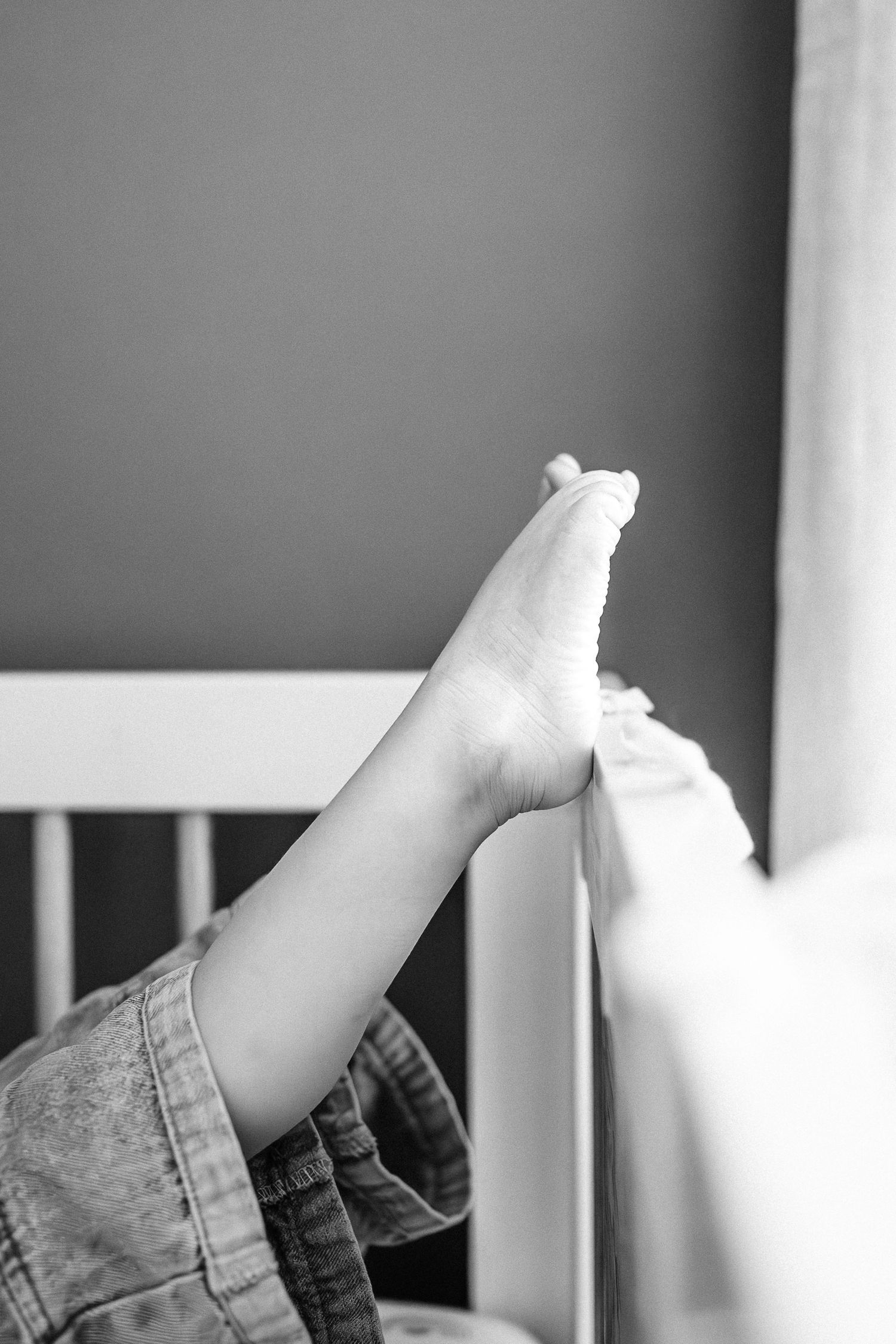 Close-up of small feet against gray background near white crib rails.