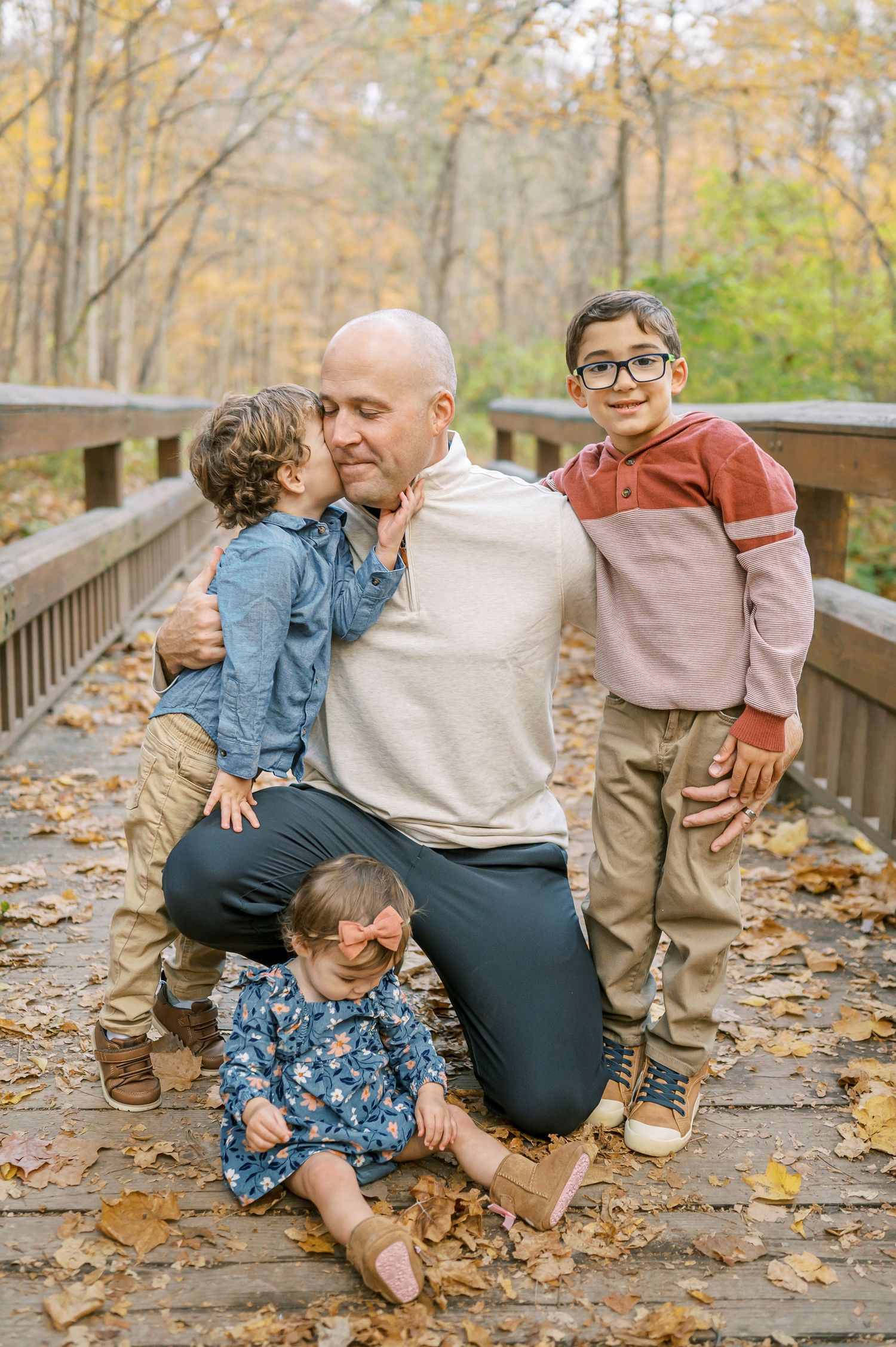 Family enjoying playful moments together on leaf-covered boardwalk in autumn woods.