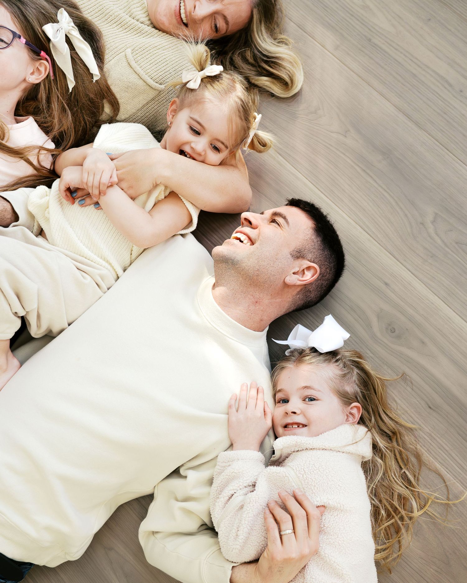 Family lying on hardwood floor wearing cream colored sweaters.