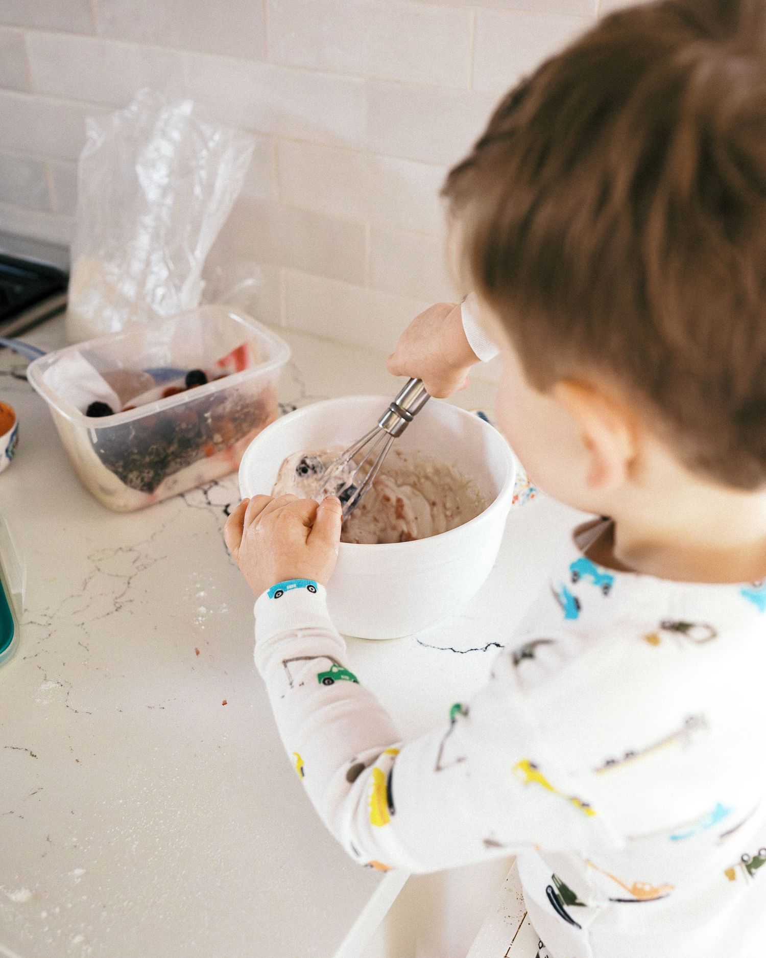 Close-up of small hands mixing ingredients in a white bowl while wearing vehicle-patterned sleeves.