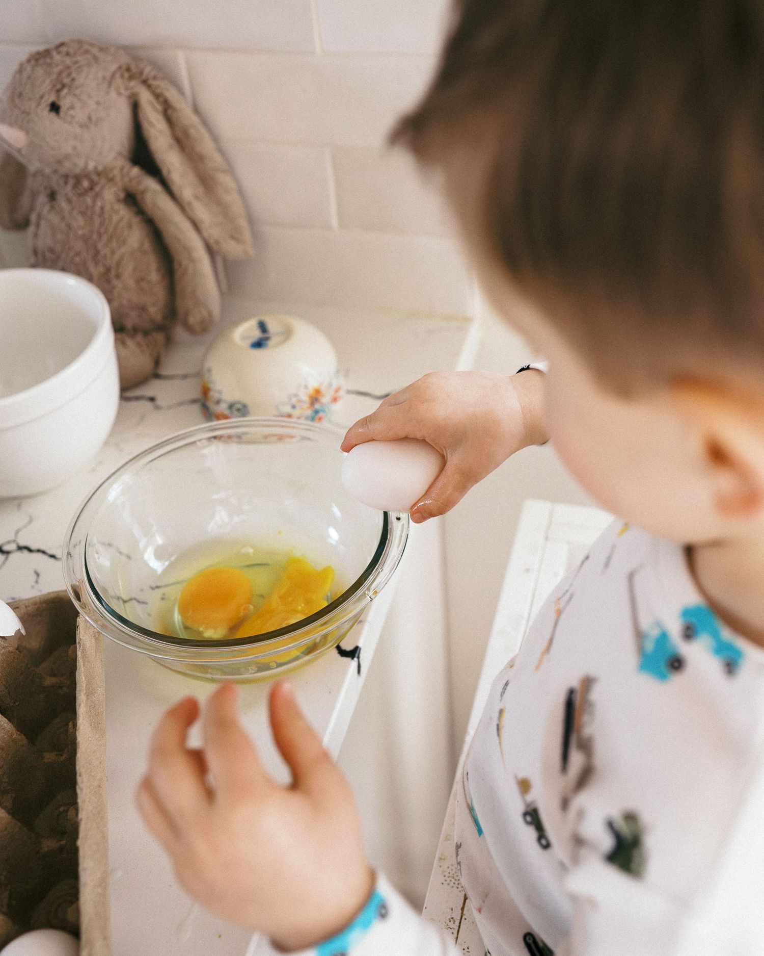 Someone breaking an egg into a clear glass bowl in a bright white kitchen.