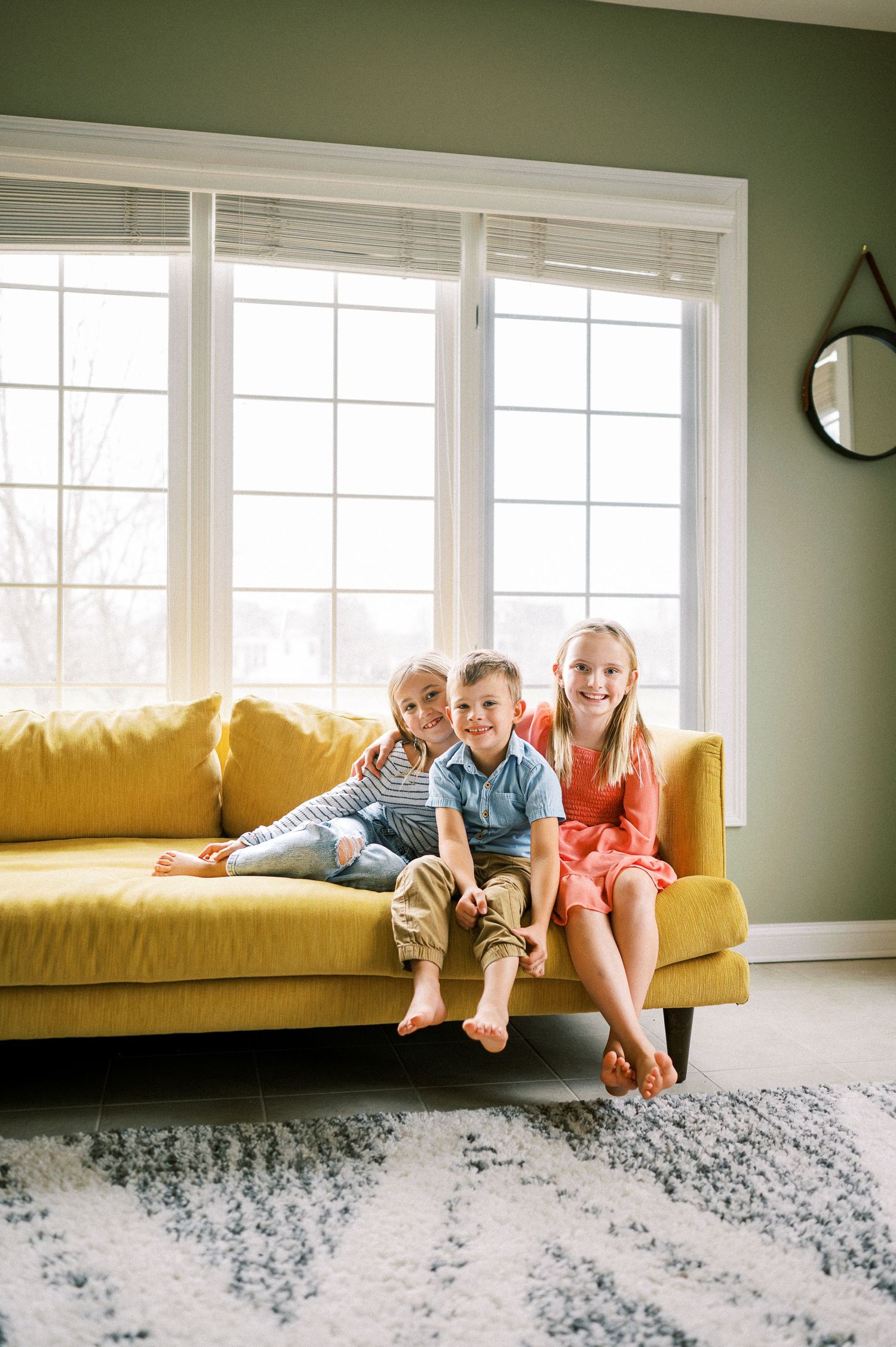 Three people relaxing together on a yellow couch with a gray patterned rug below.
