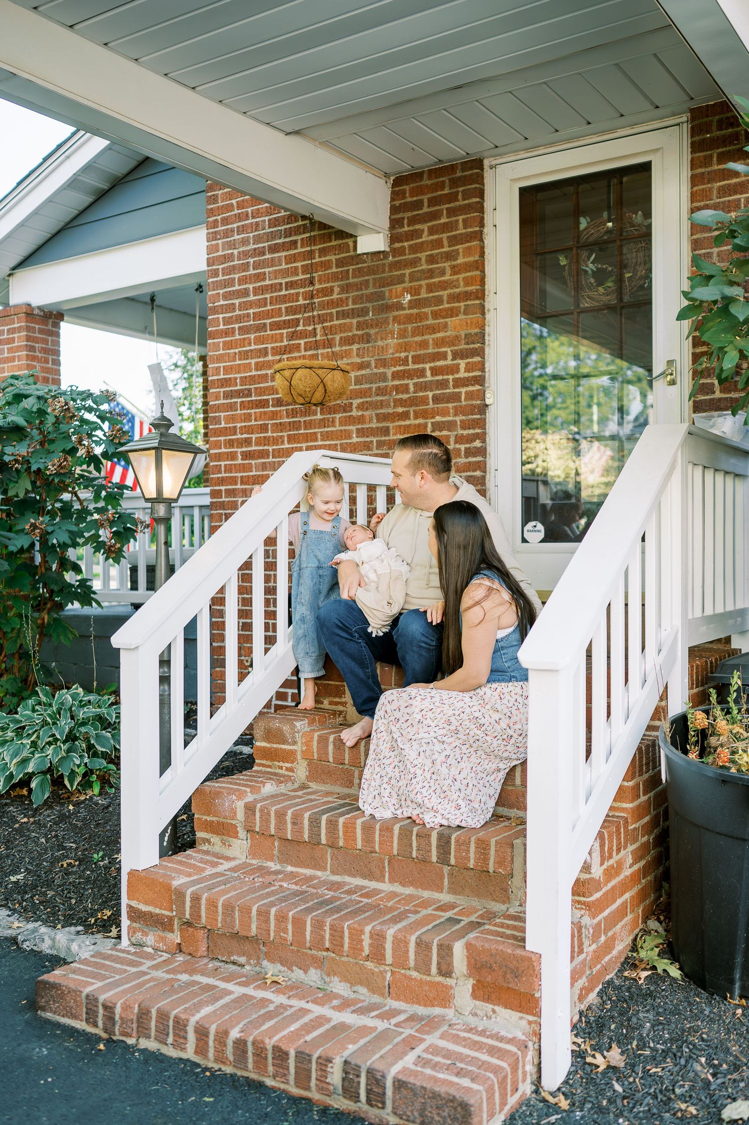 Family relaxes together on brick front porch steps of their home.