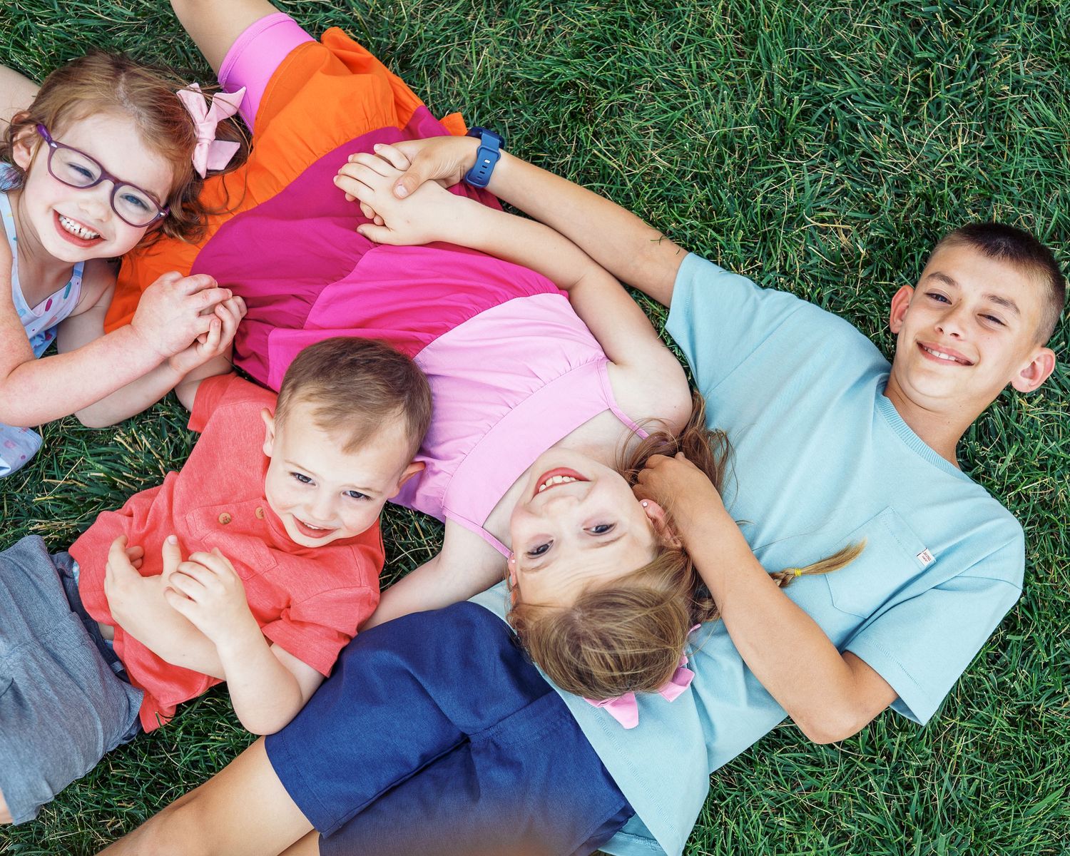 Laughing children lay together on grass during a playful outdoor moment.
