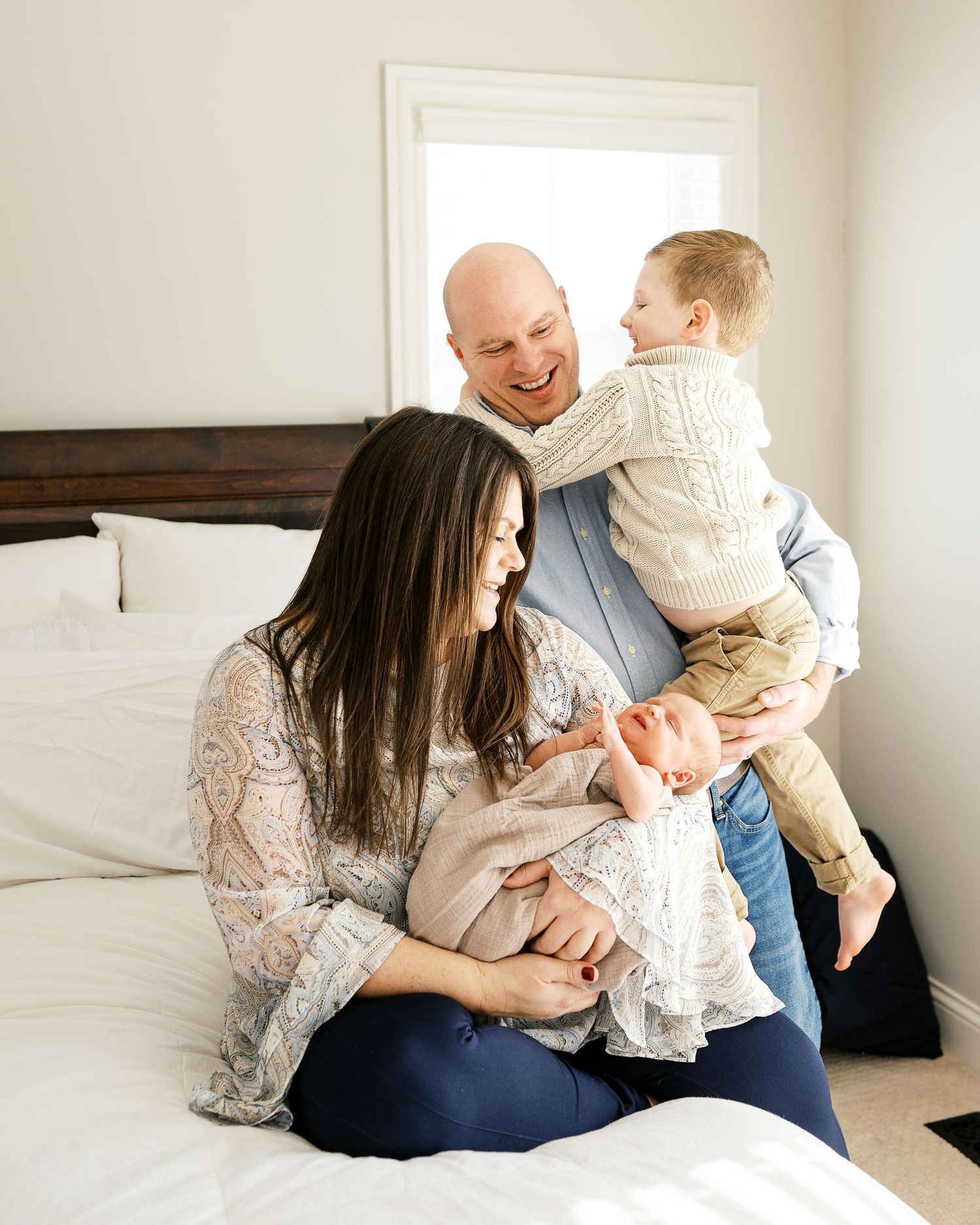 A happy family shares tender moments together while sitting on a white bed.