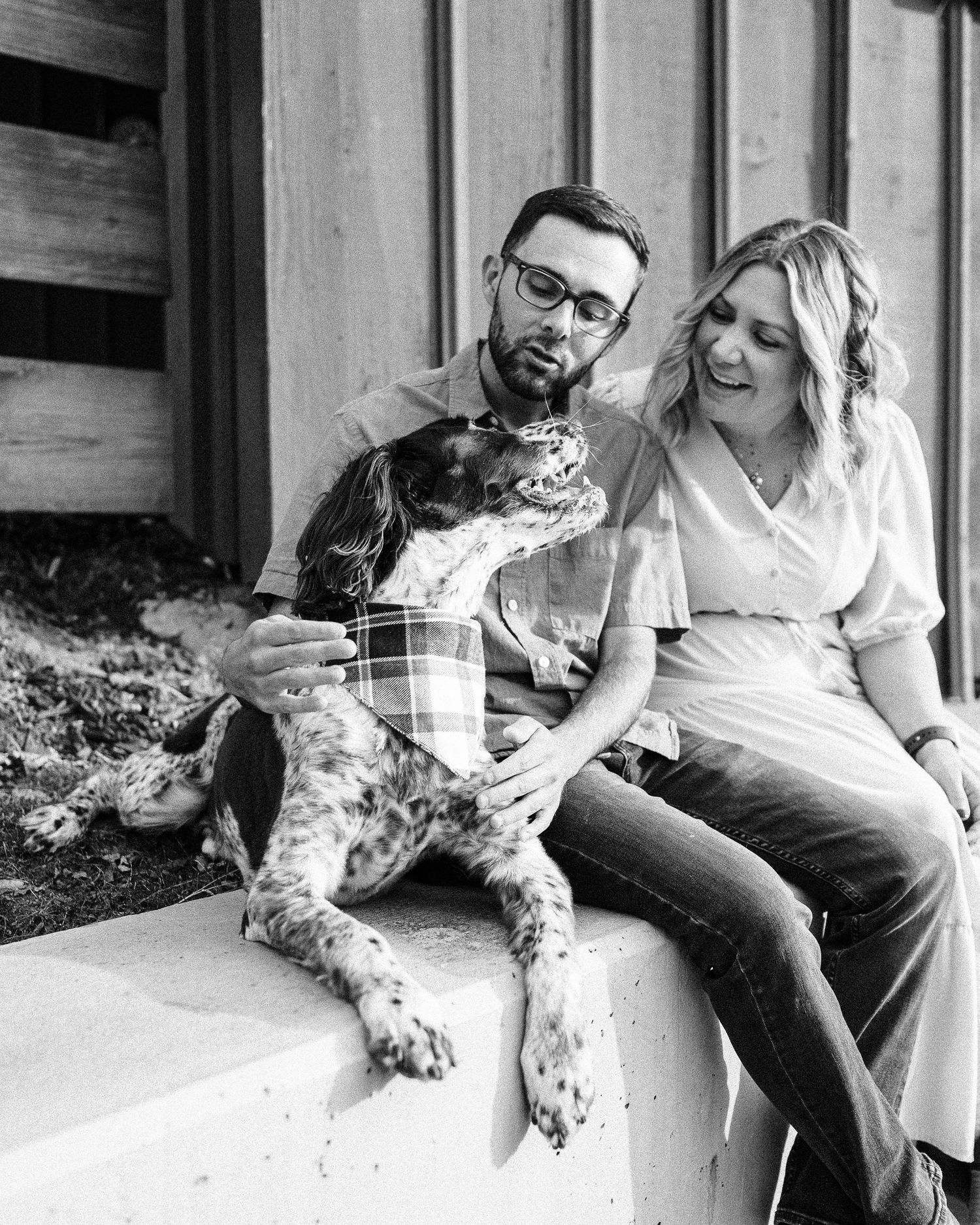Black and white photo of couple sitting on porch steps with their spotted dog.