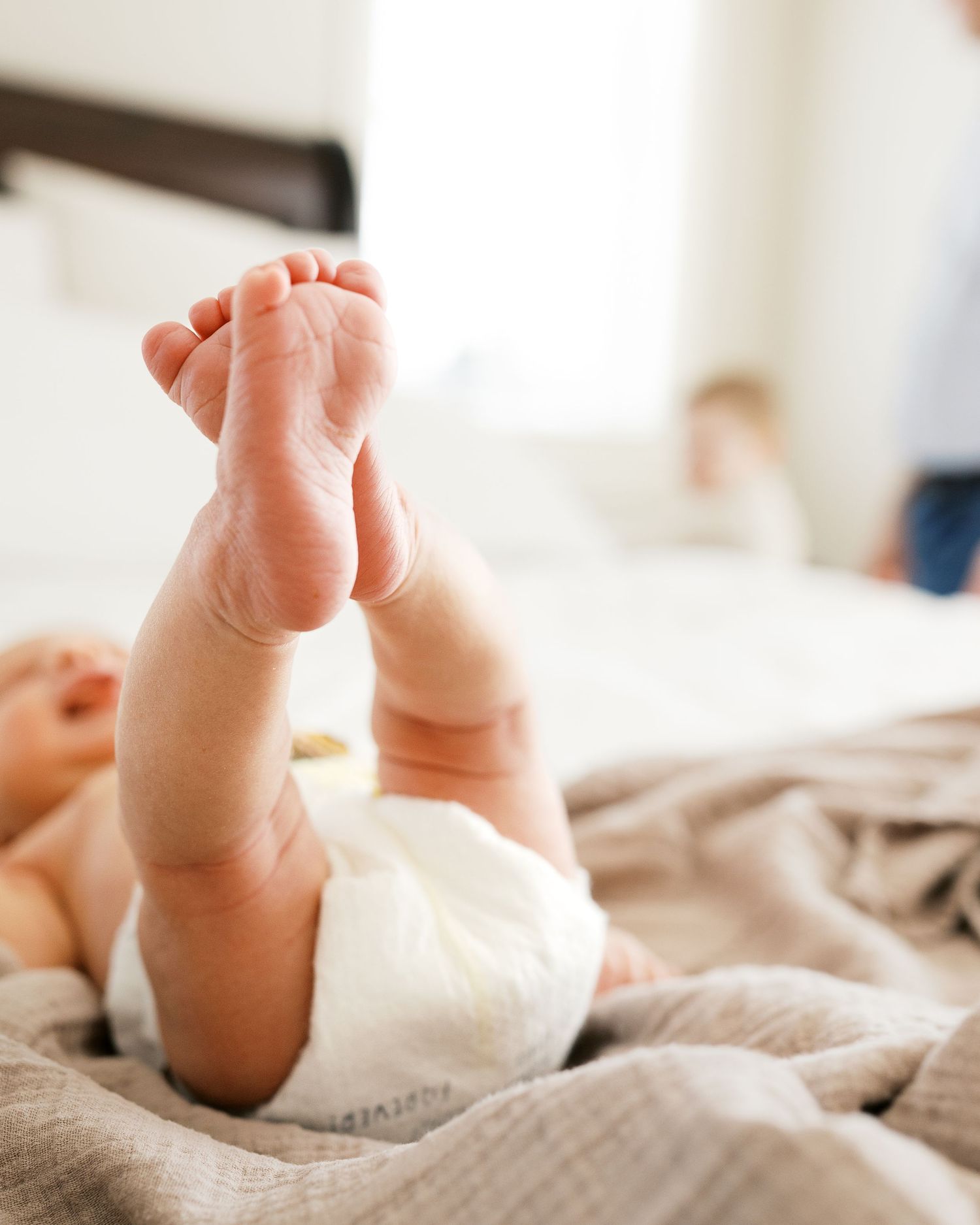 Close-up of baby feet against white bedding in soft natural light.