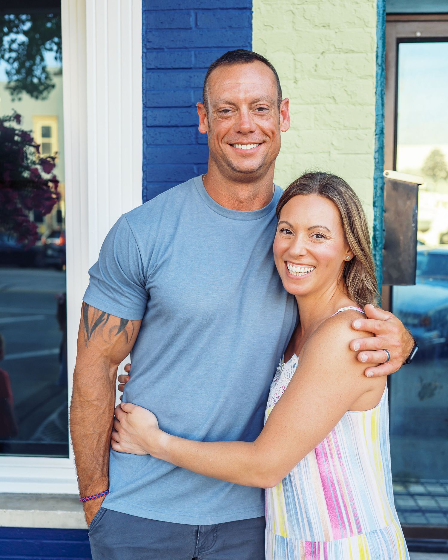 Couple embracing in front of blue and yellow painted building exterior.